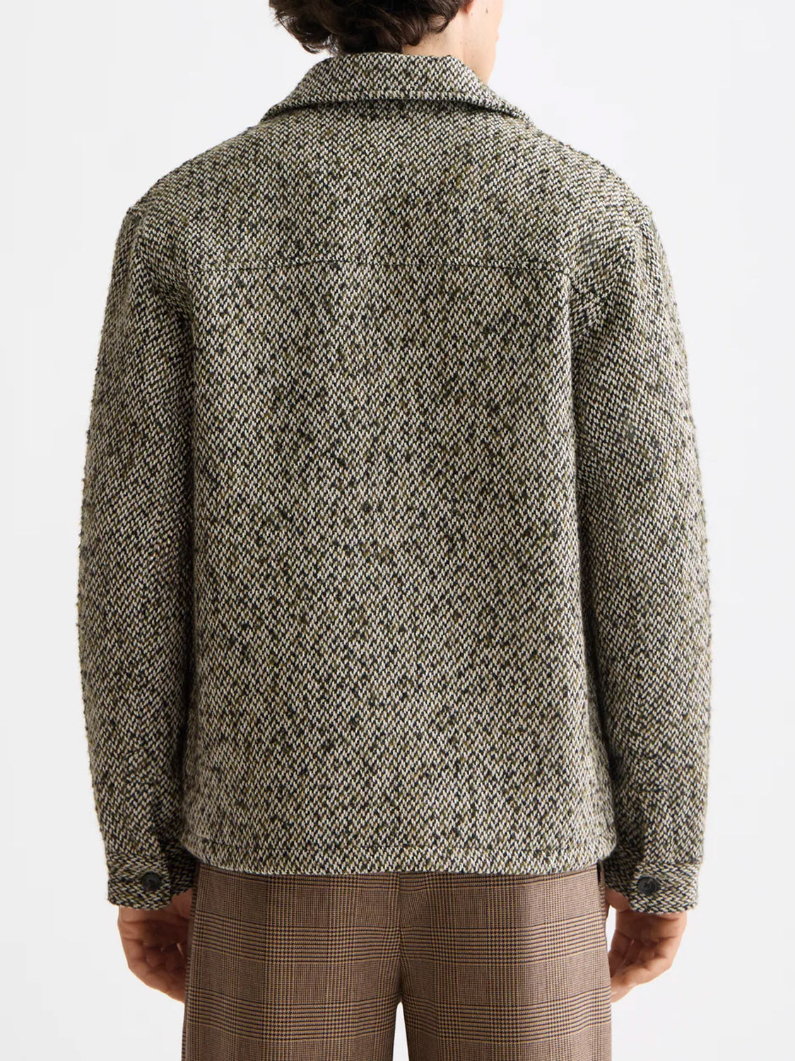 A person is seen from behind wearing the Scotch & Soda 181609 Multicolored Tweed Overshirt, featuring a collar and textured gray and black tones, paired with brown plaid pants against a plain light backdrop.