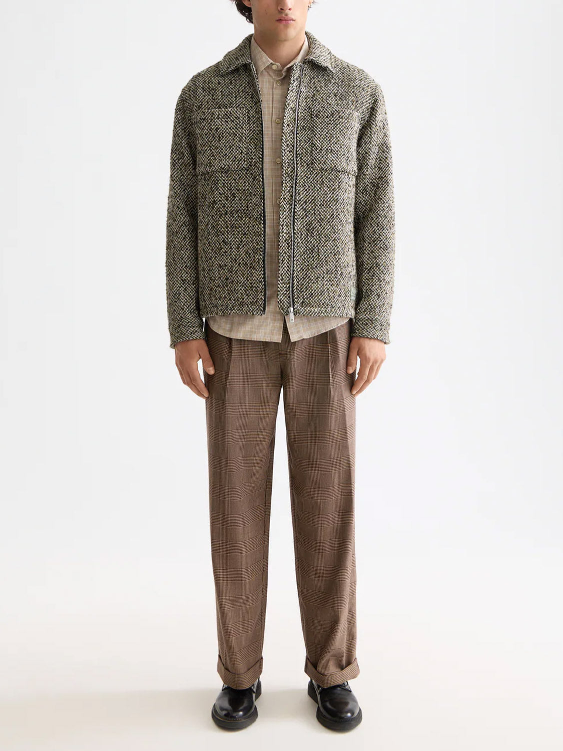 A person wearing a Scotch & Soda 181609 Multicolored Tweed Overshirt over a beige shirt, brown pleated trousers, and black shoes stands against a white background. The person's head is not shown in the frame.