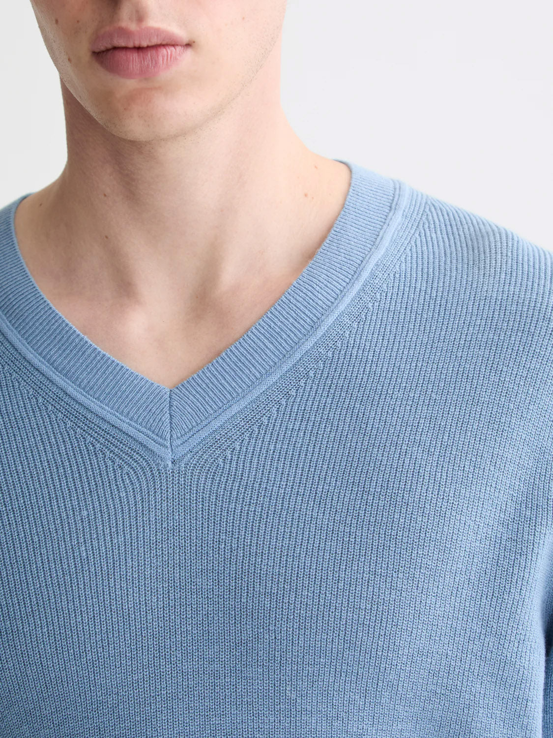 Close-up of a person wearing the Scotch & Soda 181773 Cotton Linen V-Neck Pullover, highlighting the lower face and upper chest. The image emphasizes the mid-length cut and soft knit texture of this light blue sweater.