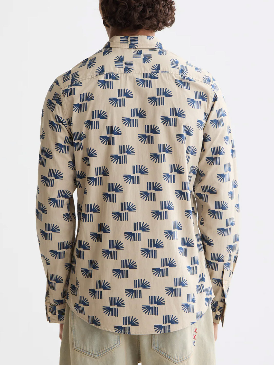 A person is pictured from behind in a Scotch & Soda 181804 Slim Fit Micro All-Over Printed Shirt with blue geometric patterns and beige tones, paired with light pants, set against a plain white background.