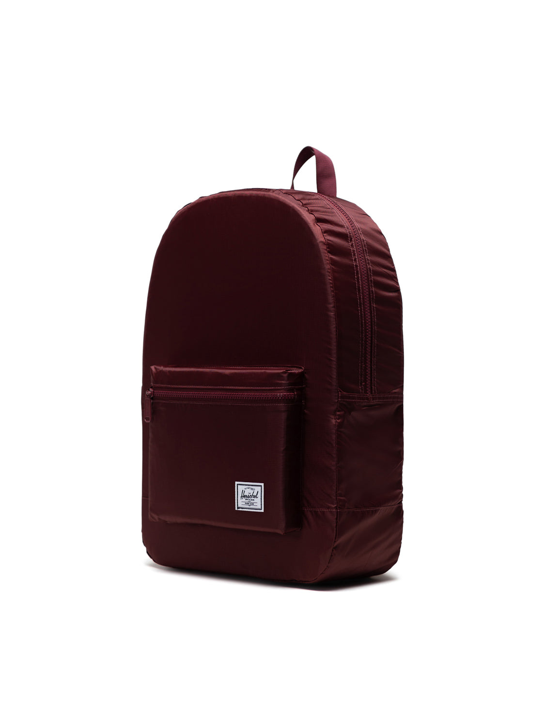 The Herschel Packable Daypack by Herschel is a maroon backpack with adjustable shoulder straps, a front zippered pocket, a small white rectangular logo patch, and a top carrying handle, displayed on a plain white background.