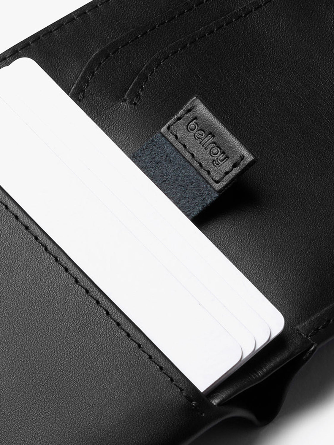 Close-up of a Bellroy Note Sleeve Wallet in black, with three white cards partially visible in the pocket. Features a small embossed tab and built-in RFID protection for added security.