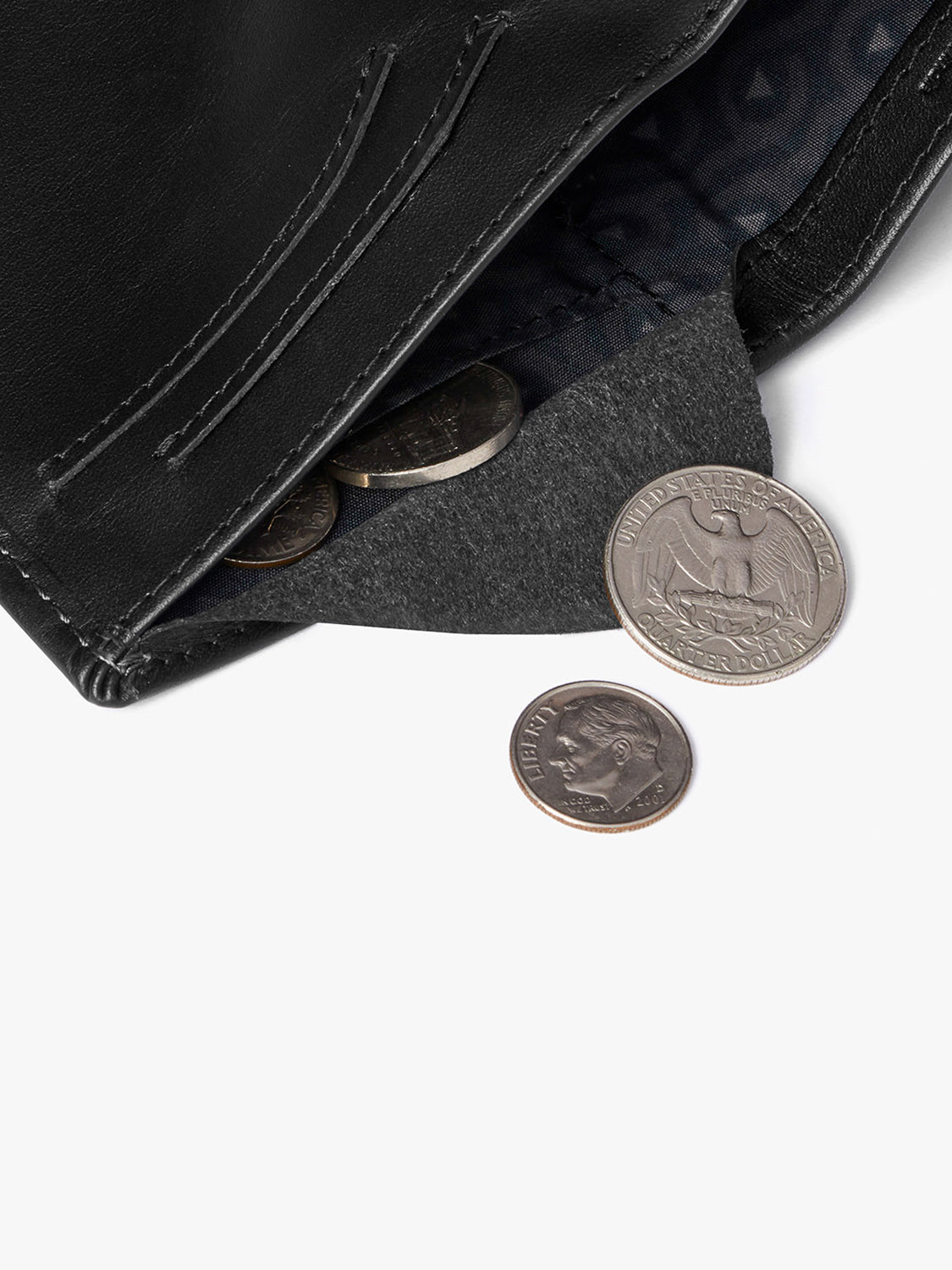 The Bellroy Note Sleeve Wallet displays its inner lining as coins, including a quarter and a dime, spill onto a white surface. This slim billfold is ideal for organizing essentials while traveling.