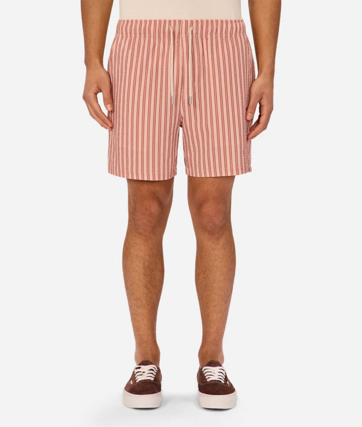 A person wearing the Industrie Berkeley Swim Short in red and white vertical stripes with a drawstring, paired with a beige top and brown sneakers with white laces, stands against a plain background.