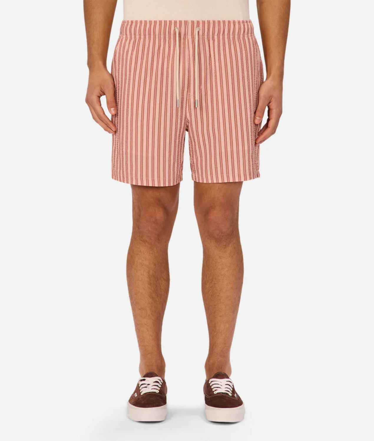 A person wearing the Industrie Berkeley Swim Short in red and white vertical stripes with a drawstring, paired with a beige top and brown sneakers with white laces, stands against a plain background.