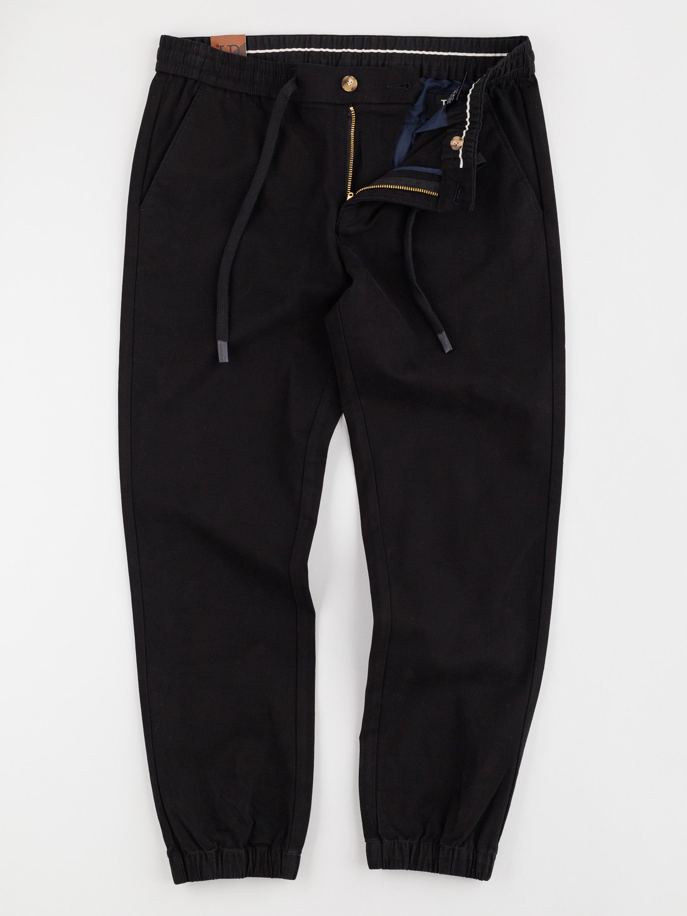 The Dyker Cotton Twill Drawstring Jogger by ID Menswear is designed with an open zipper, drawstring, button closure, ankle elastic cuffs, front pockets, and an elastic waistband with inner decorative stitching.