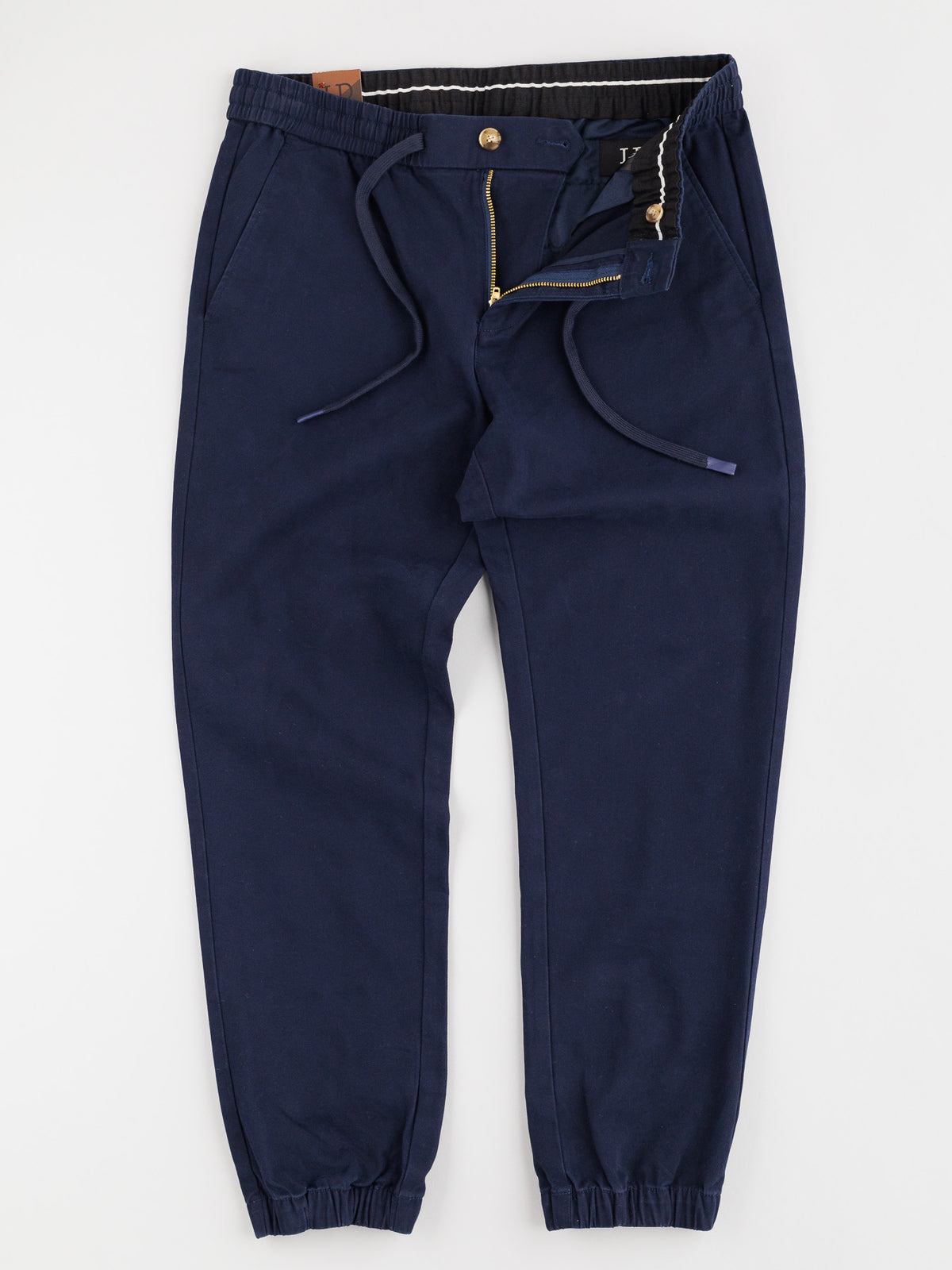 The Dyker Cotton Twill Drawstring Jogger by ID Menswear is a navy blue jogger with zipper fly, elastic waistband and cuffs, and side pockets. Laid elegantly flat on a white background, it offers comfort and style.