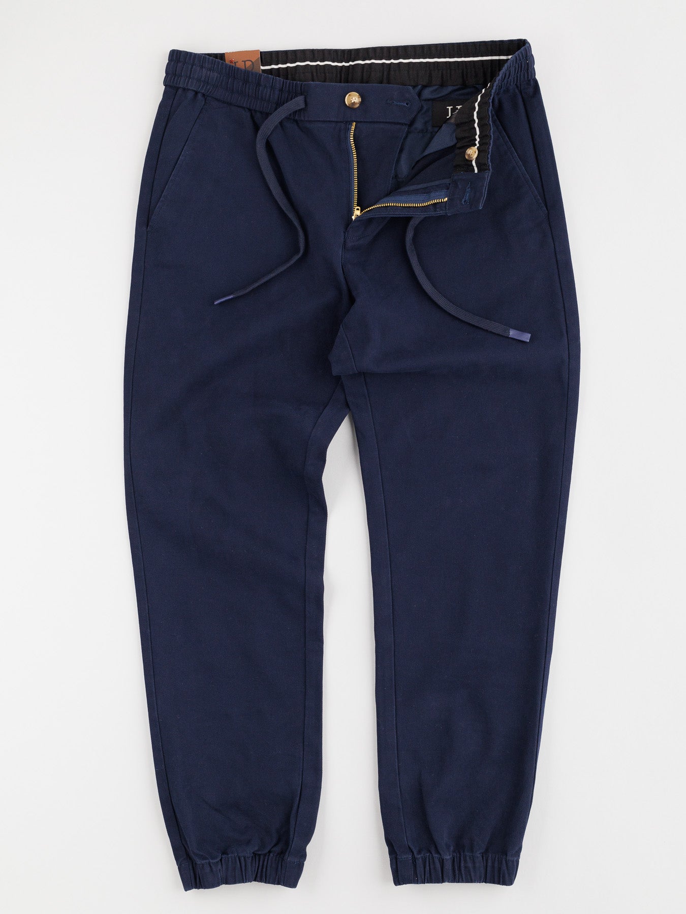 The Dyker Cotton Twill Drawstring Jogger by ID Menswear is a navy blue jogger with zipper fly, elastic waistband and cuffs, and side pockets. Laid elegantly flat on a white background, it offers comfort and style.