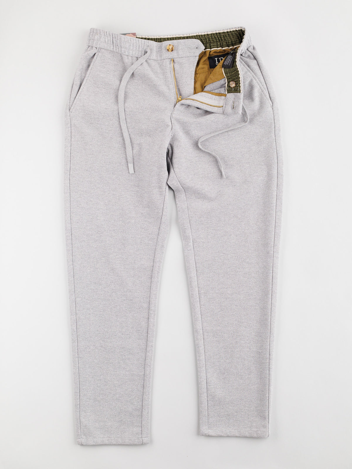 The Brighton Brushed Polyester Rayon Pant by ID Menswear features a light grey drawstring design with an elastic waist, side pockets, and partially open fly revealing a green interior with tan lining. Its displayed flat on a white background.