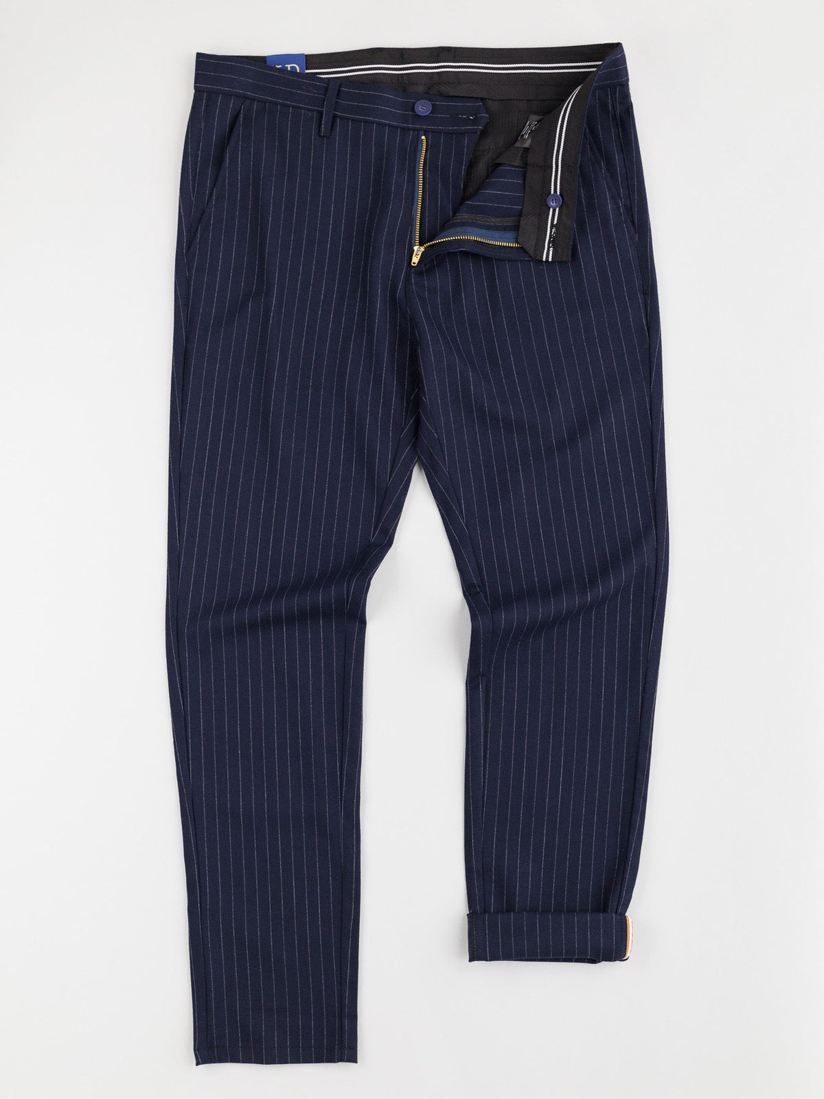 The Hudson Wool Blend Pin Stripe Pant by ID Menswear features a dark blue pinstripe design in a mid-rise, slim-fit crafted from premium wool blend. It has belt loops, a partially open zipper, and a contrasting striped pattern lining for added elegance.