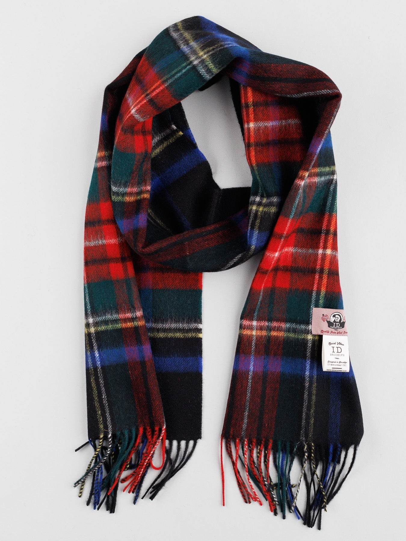 The ID Menswear Wool Plaid Scarf with Self-Fringed Ends, featuring a vibrant red, blue, green, and black tartan pattern and a label near one end, is the perfect winter wardrobe addition for cold days.