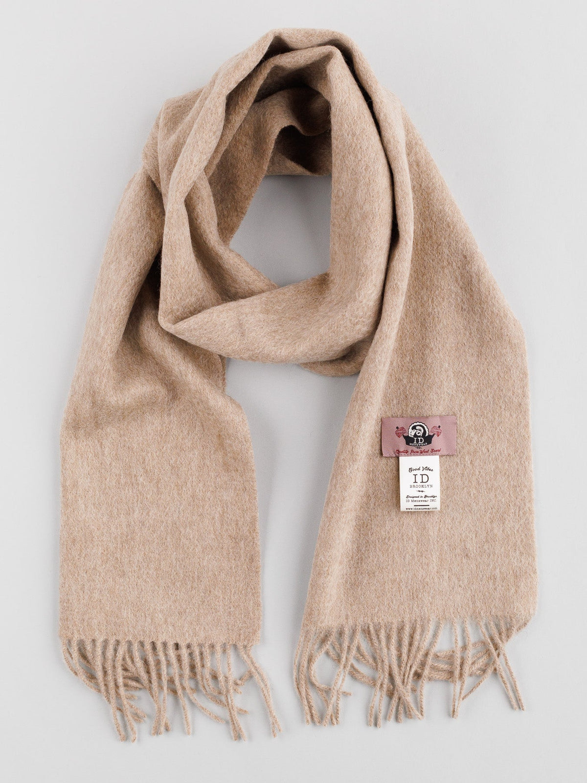 A beige Wool Scarf with Self-Fringed Ends from ID Menswear is displayed on a plain background, highlighting its classic design. It includes a pink logo tag and a white product info tag, making it an essential winter accessory.