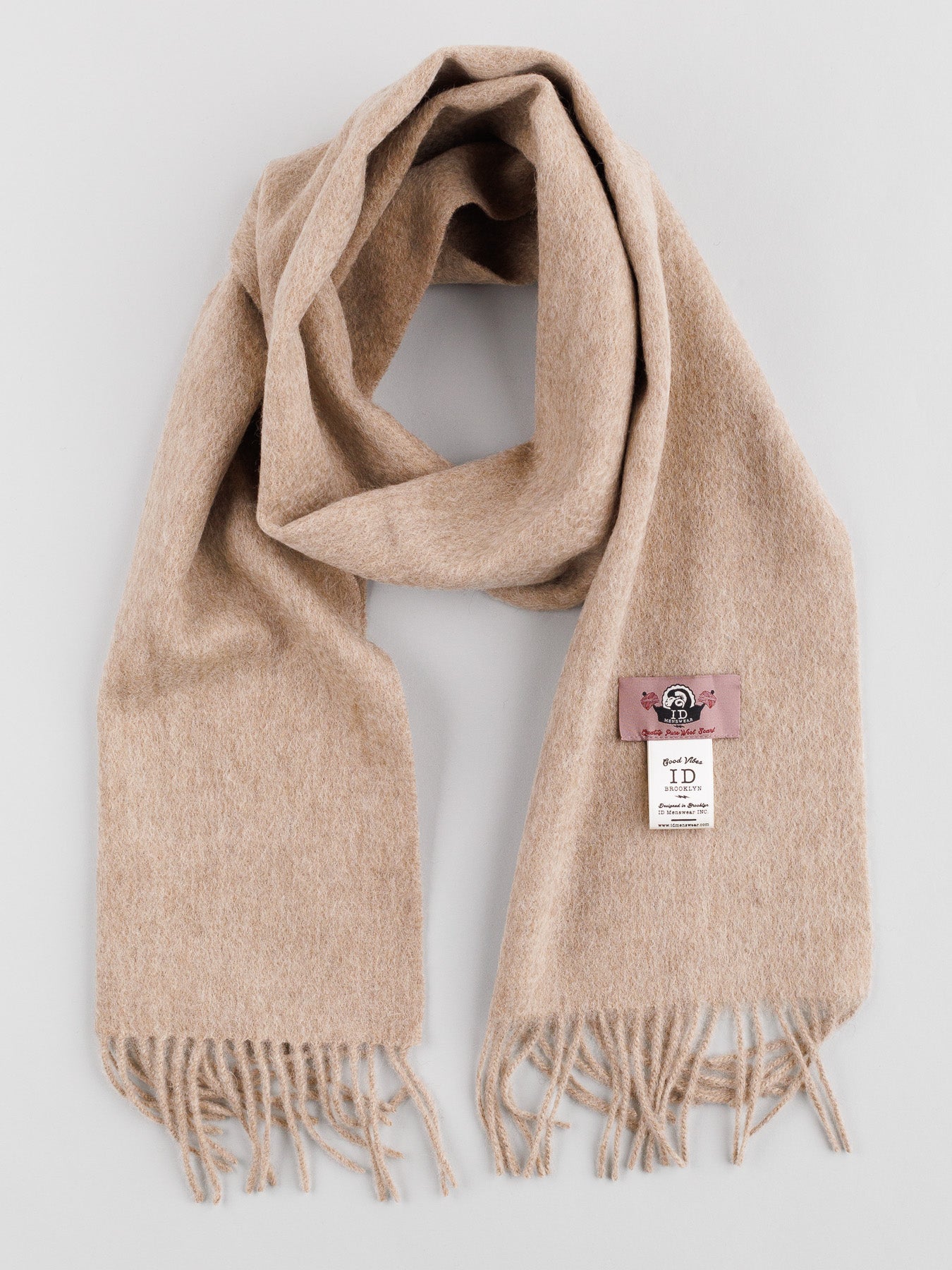 A beige Wool Scarf with Self-Fringed Ends from ID Menswear is displayed on a plain background, highlighting its classic design. It includes a pink logo tag and a white product info tag, making it an essential winter accessory.