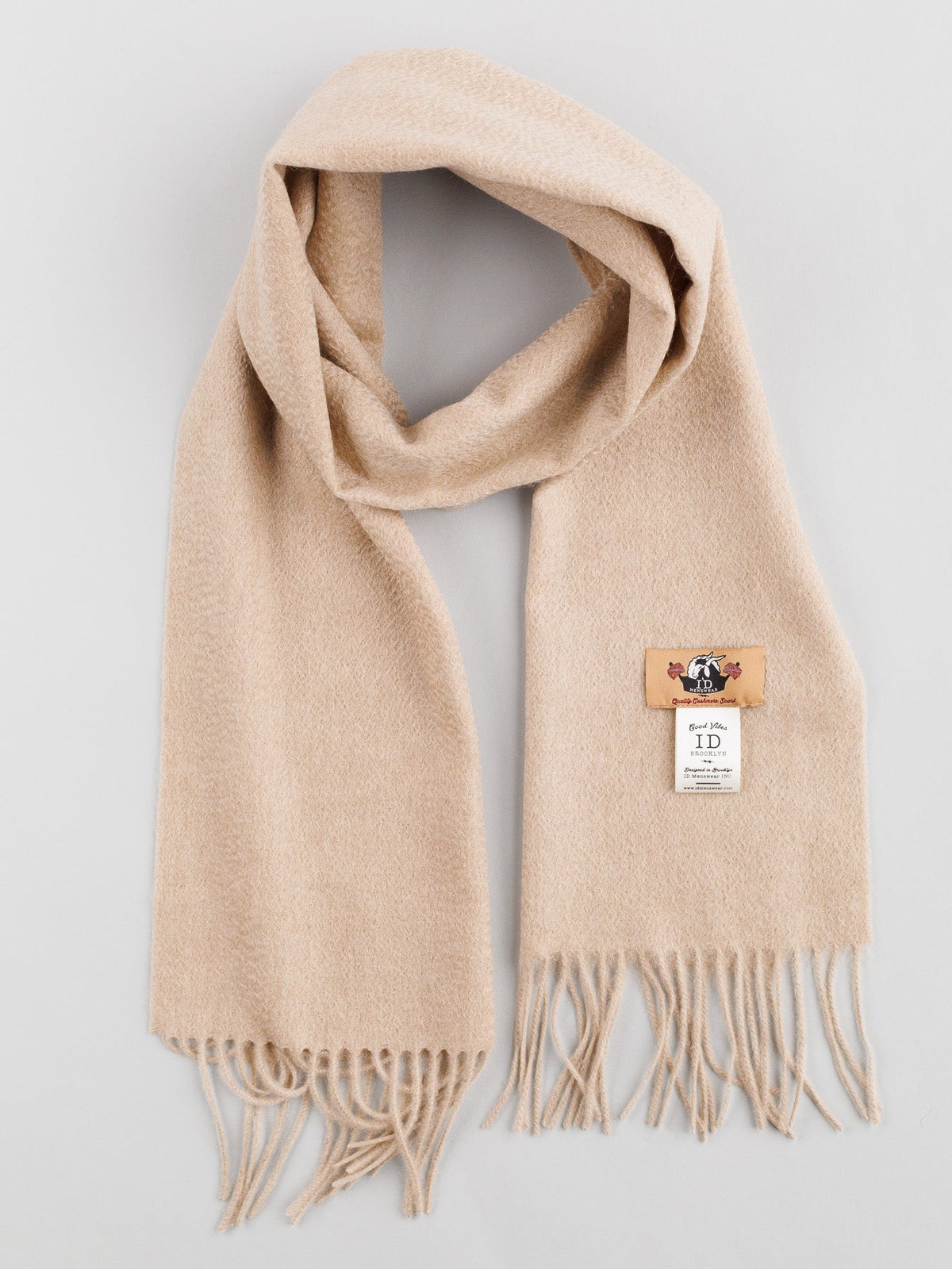 The Cashmere Scarf with Self-Fringed Ends by ID Menswear, in beige wool and adorned with a logo label, exudes timeless elegance. Draped in a graceful loop on a neutral gray background, this exquisite piece is perfect for your winter wardrobe.