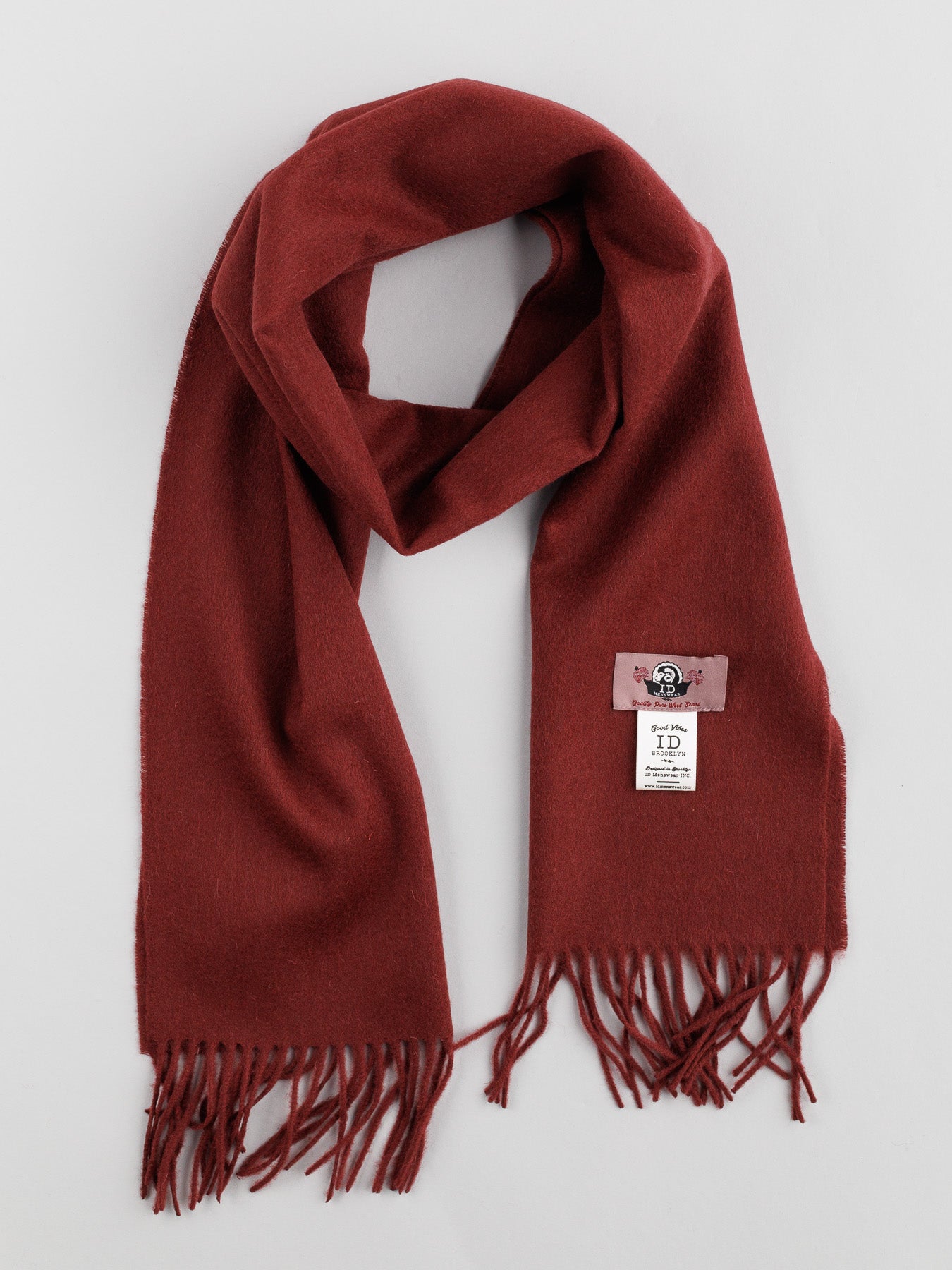 The Wool Scarf with Self-Fringed Ends by ID Menswear is showcased on a light gray backdrop, featuring a sewn-on label with a cartoon motif that brings a playful vibe to this timeless winter piece.