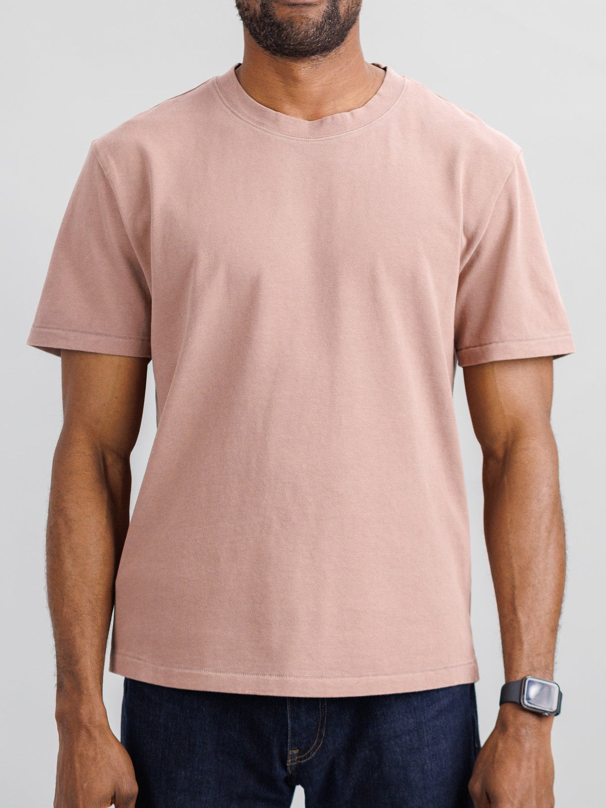 A person wearing the Freeman Organic Vintage Wash Tee by ID Menswear, paired with dark jeans, stands with hands relaxed at their sides. A smartwatch is on their left wrist, set against a plain light-colored background.