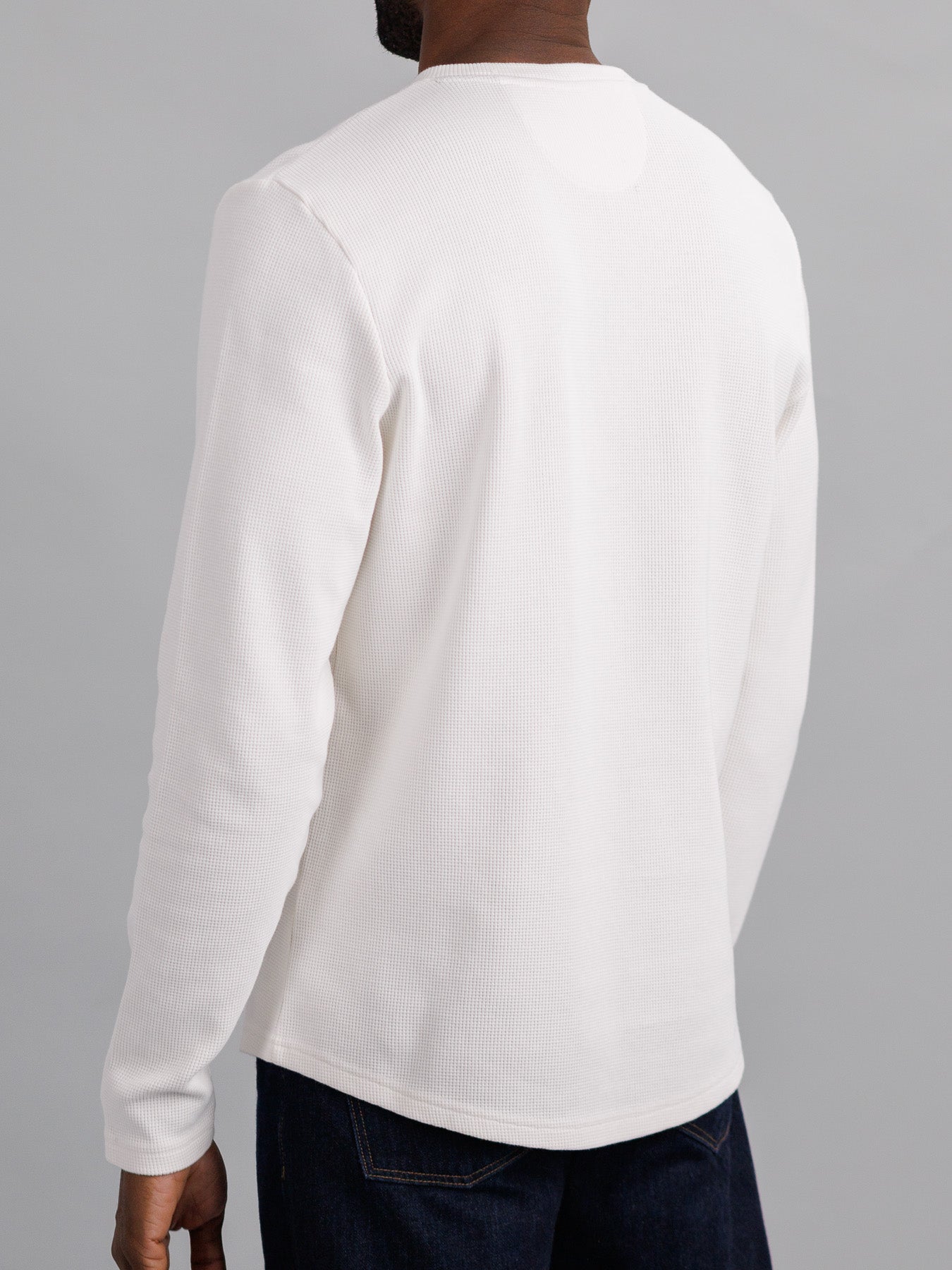 A person in a white ID Menswear Freestyle Waffle Knit Henley and dark jeans is shown from the back against a plain gray background. The cotton-spandex blend offers comfort and mobility, ideal for casual outings.