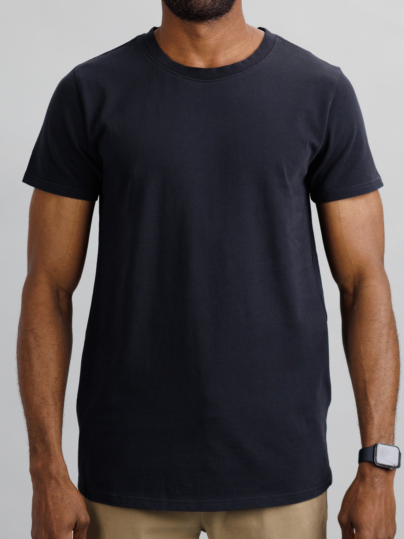 A person wearing an ID Menswear City Organic Cotton Tee and khaki pants stands against a plain background, showcasing a sleek smartwatch on their left wrist.