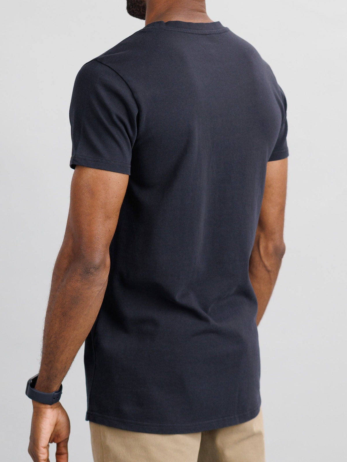 A rear view of someone in a slim fit City Organic Cotton Tee by ID Menswear, light brown pants, and a black wristwatch, set against a neutral background.