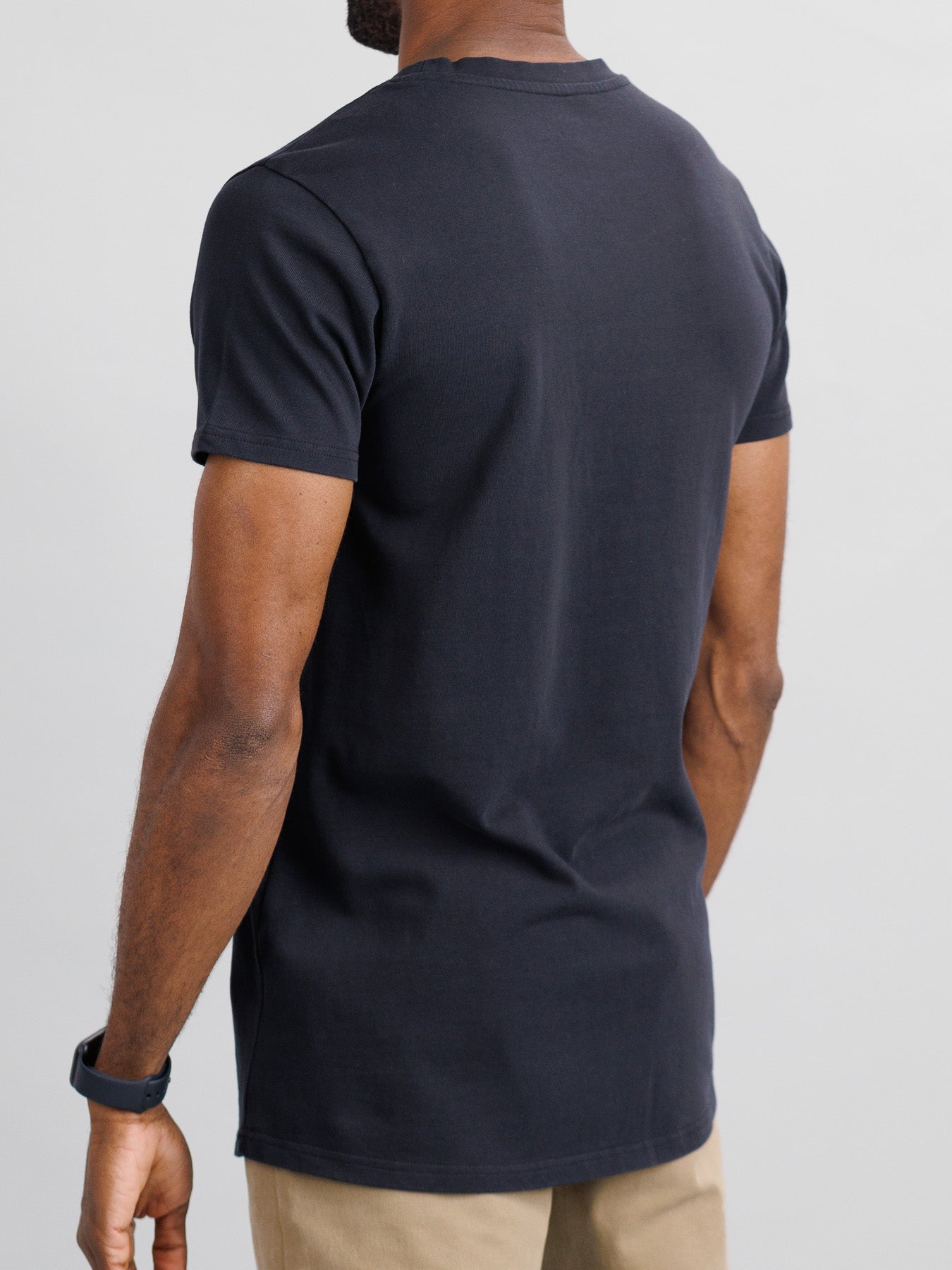 A rear view of someone in a slim fit City Organic Cotton Tee by ID Menswear, light brown pants, and a black wristwatch, set against a neutral background.