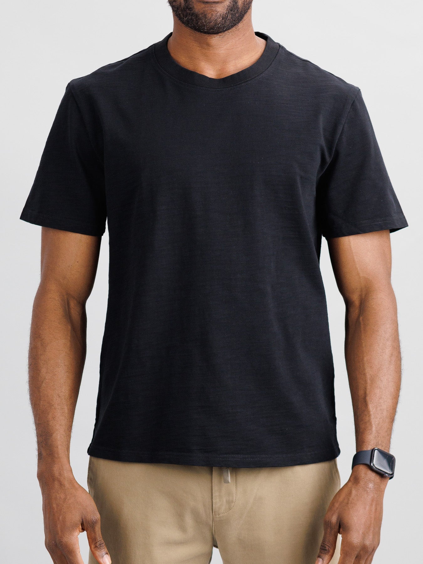A man in an ID Menswear Big Flip Slub Yarn Cotton Tee and beige pants stands against a neutral background. He sports a boxy fit look, complemented by a black smartwatch on his left wrist.