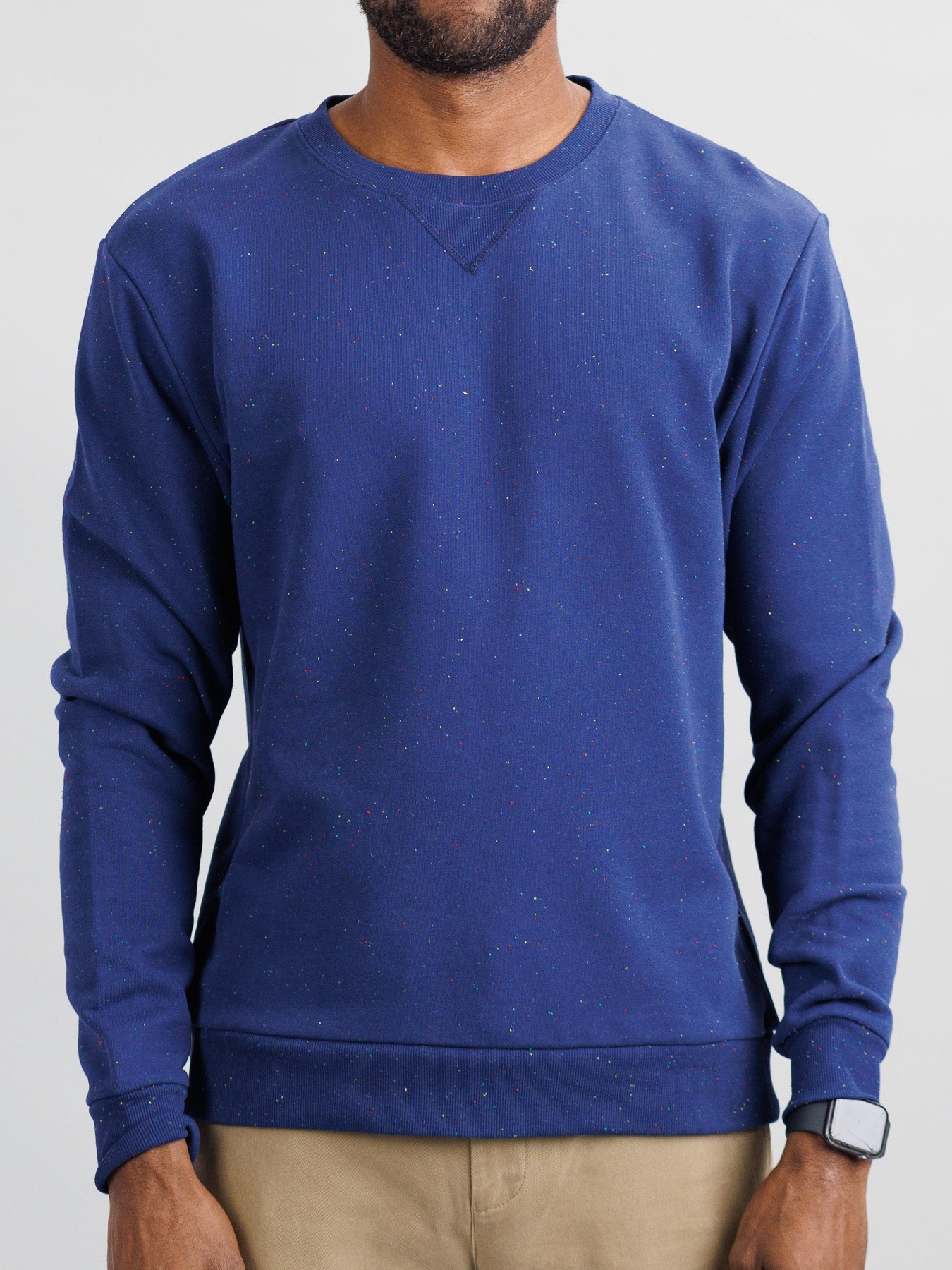 Against a plain background, a person wears the ID Menswear Stardust Speckled Sweatshirt with multicolored specks that exude subtle charm. Light brown pants enhance the look, while a smartwatch adds modern flair. Their unseen face is outshone by the sweatshirts regular fit allure.