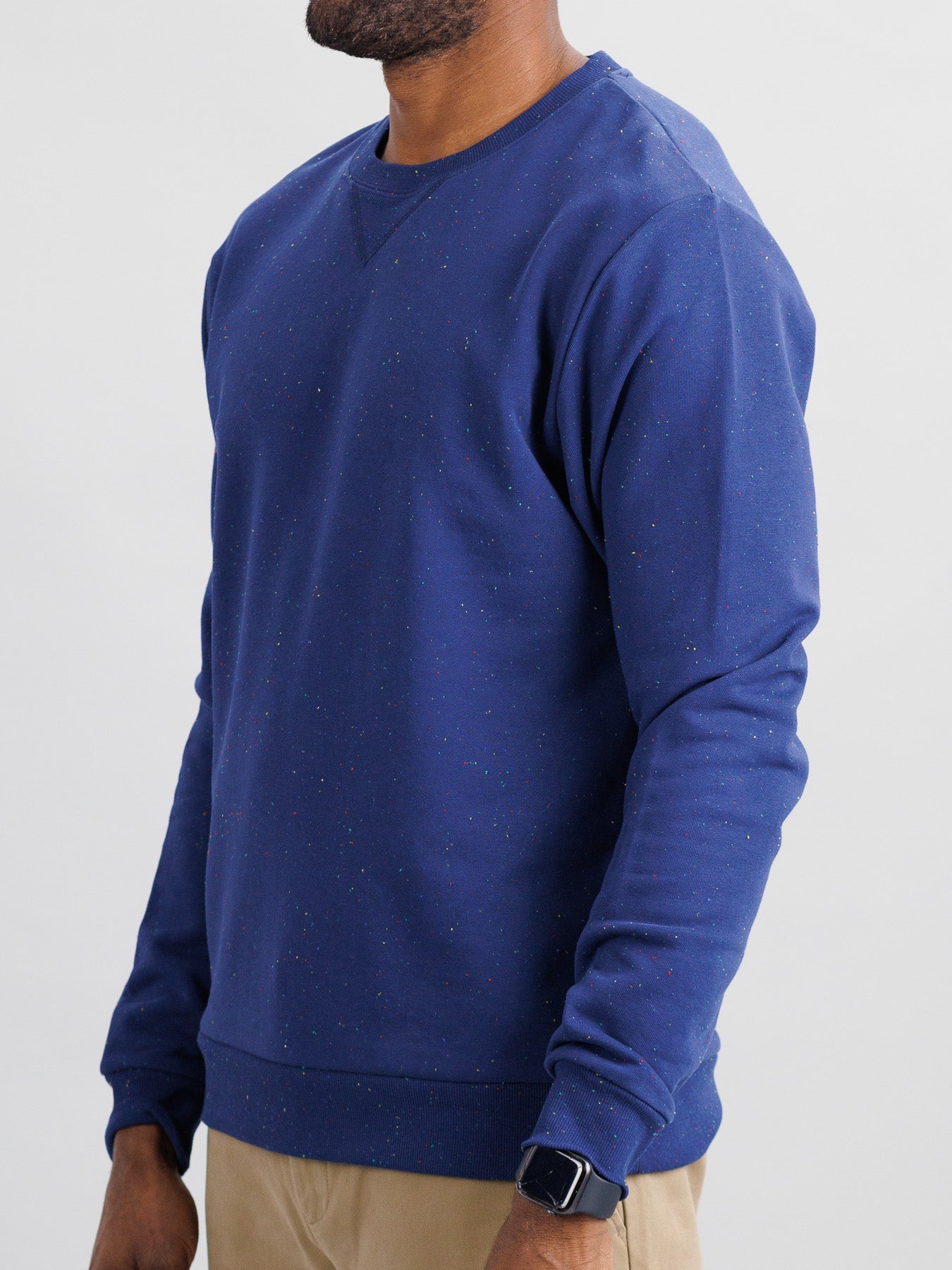 Dressed in ID Menswears Stardust Speckled Sweatshirt made from speckled cotton yarn and paired with beige pants, a person wears a watch on their wrist against a plain white background.