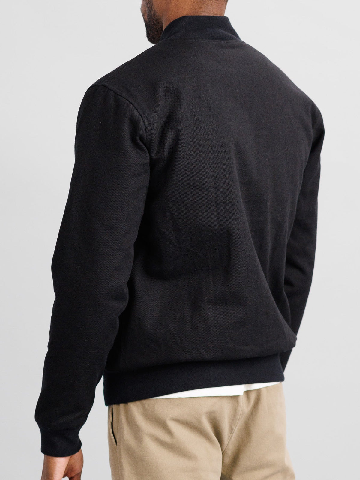 A person is shown from the back wearing the Yonkers Cotton Canvas Jacket by ID Menswear, featuring subtle quilting and a ribbed hem for comfort and style. They pair it with beige pants against a plain white background.