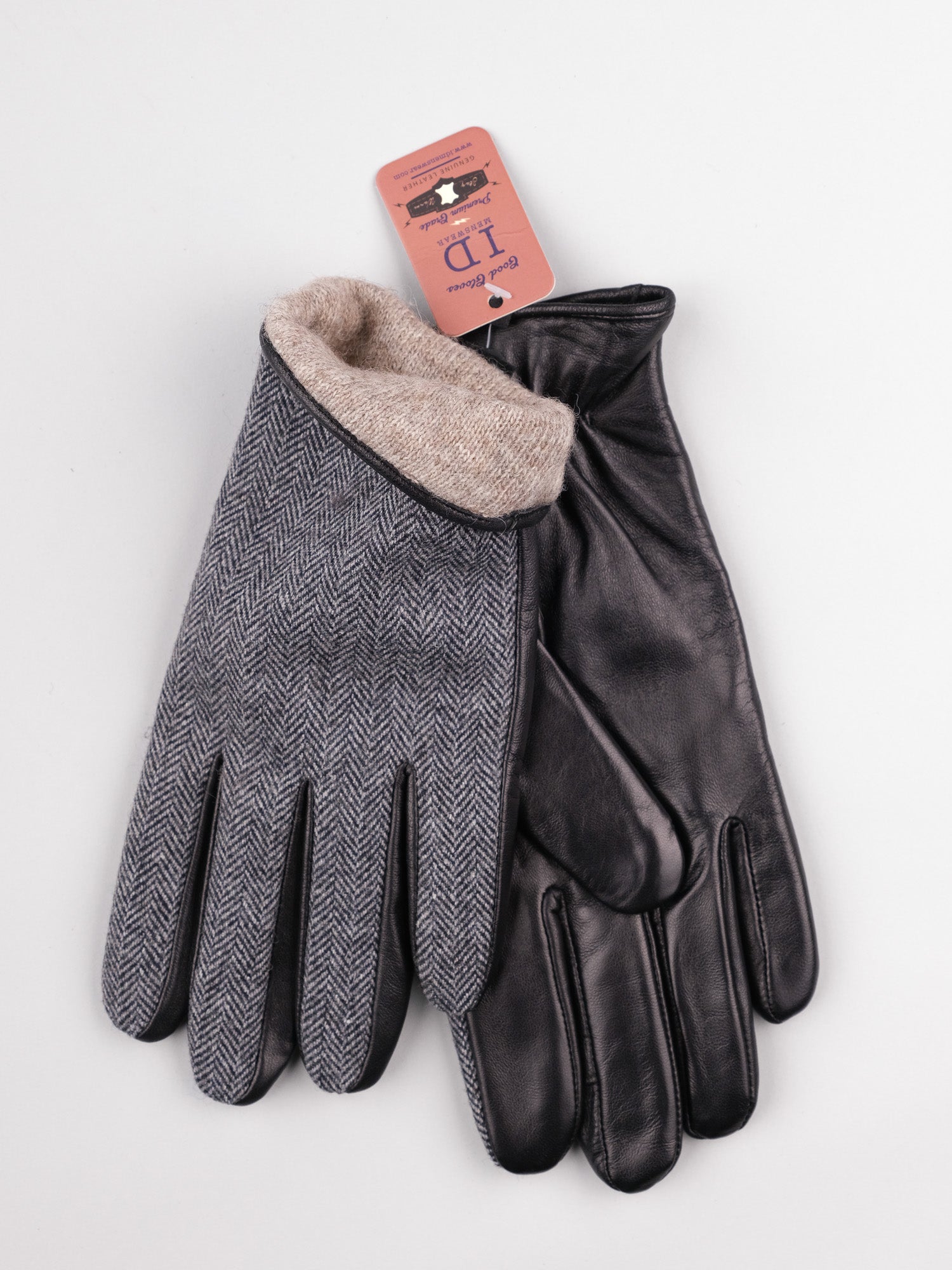 The Nordic Tweed Leather Gloves from ID Menswear feature one black sheepskin leather glove and one gray herringbone fabric glove with a beige lining. A pink tag with sizing and brand details is attached to the fabric glove, elegantly displayed on a light gray surface.
