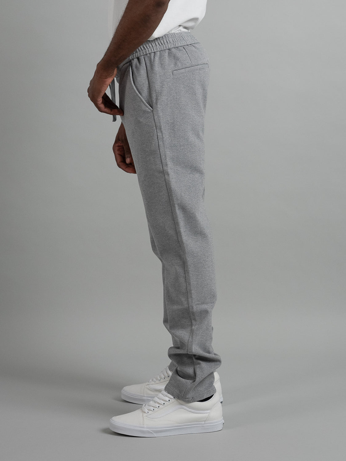 A person in profile wears ID Menswears Brighton Brushed Polyester Rayon Pant in light gray, paired with white sneakers against a plain gray backdrop. These relaxed-fit joggers feature an elastic waist and side pockets for comfort and style.