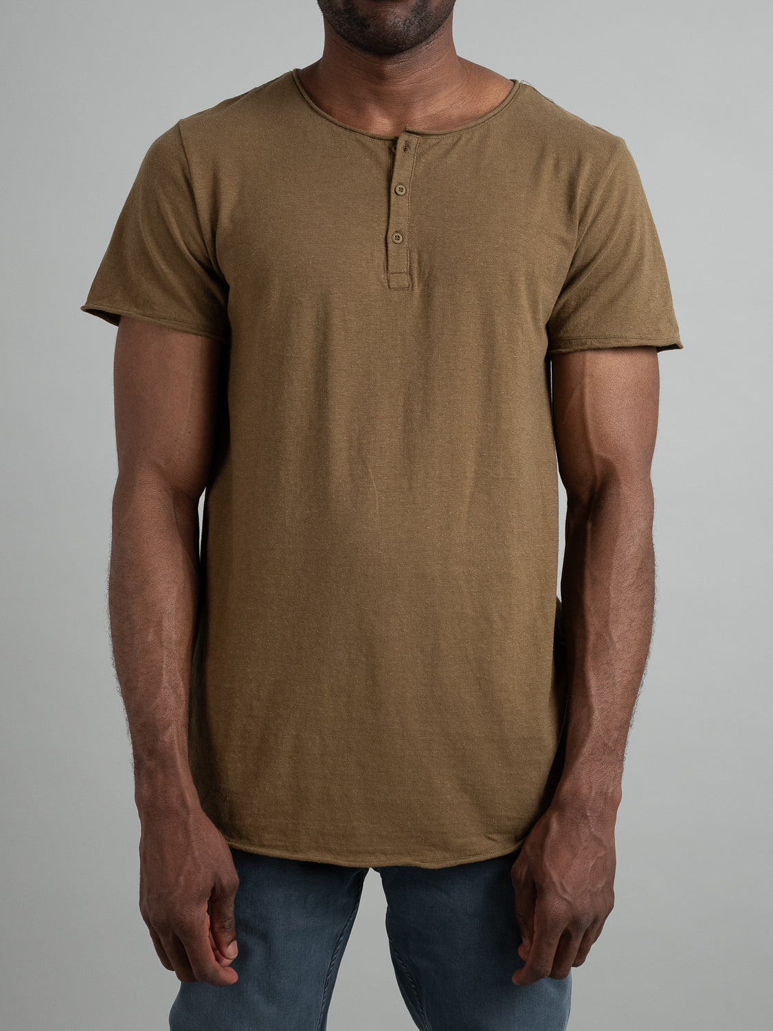 A person stands against a plain gray background, wearing an ID Menswear Legend Hemp Cotton Rolled Neck Henley and classic blue jeans. Their arms rest naturally by their sides, while their face remains hidden from view.