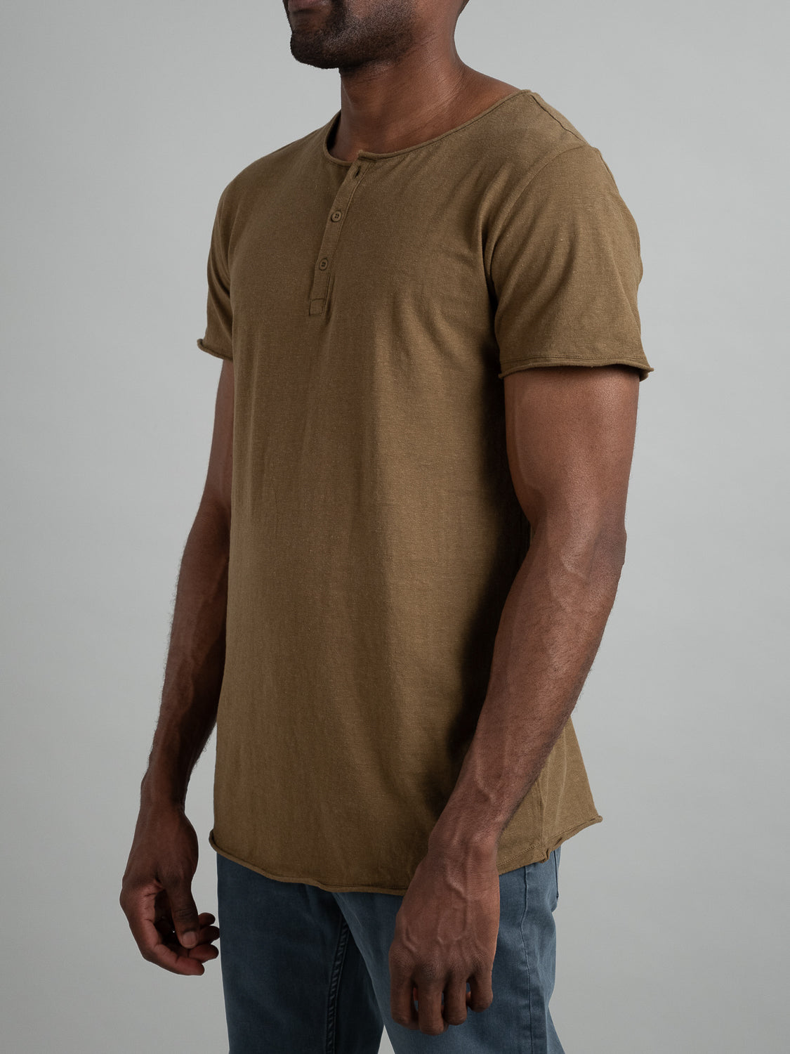 A man wearing the Legend Hemp Cotton Rolled Neck Henley in brown by ID Menswear, paired with blue jeans, stands against a plain gray background.