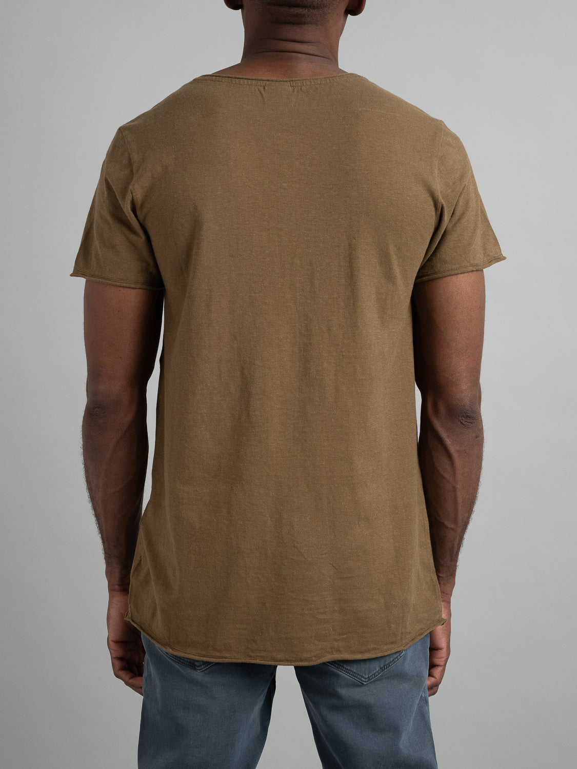 A person in a brown ID Menswear Legend Hemp Cotton Rolled Neck Henley and blue jeans stands with their back to the camera against a light gray background.