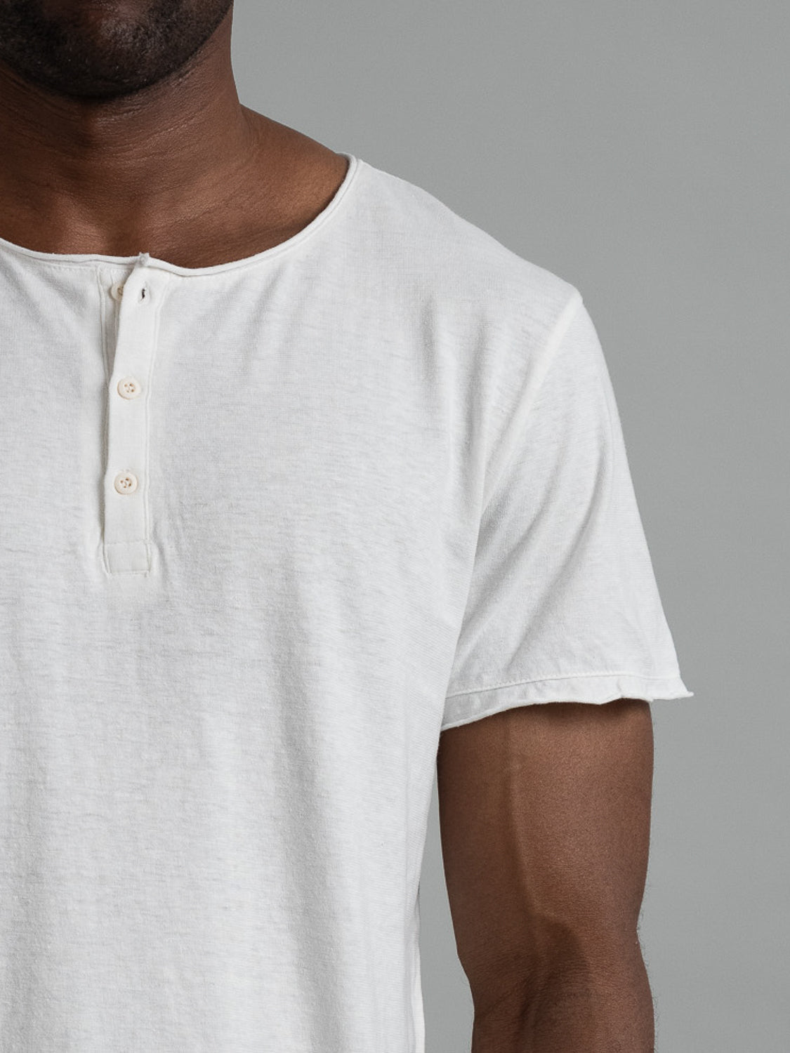 A person wearing the Legend Hemp Cotton Rolled Neck Henley by ID Menswear, a white short-sleeve shirt with three buttons crafted from breathable organic cotton, is shown against a plain gray background. The image focuses on the upper half of the shirt, keeping the face out of view.