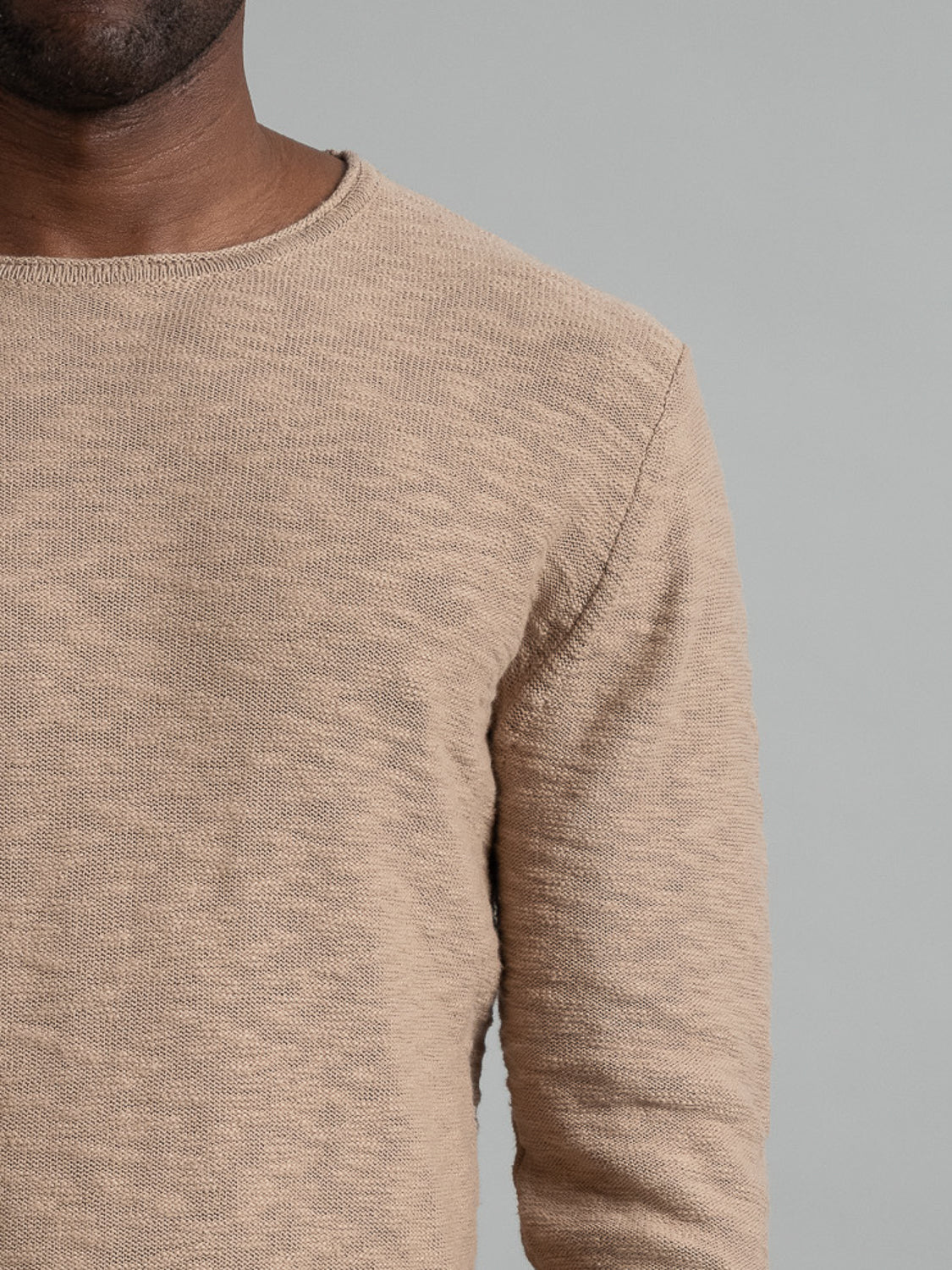 A close-up features a person in the ID Menswear beige Havana Slub Yarn Sweater Tee, showcasing its premium textured knit and simple round neckline. The left side of their face is partially obscured against a grey background.