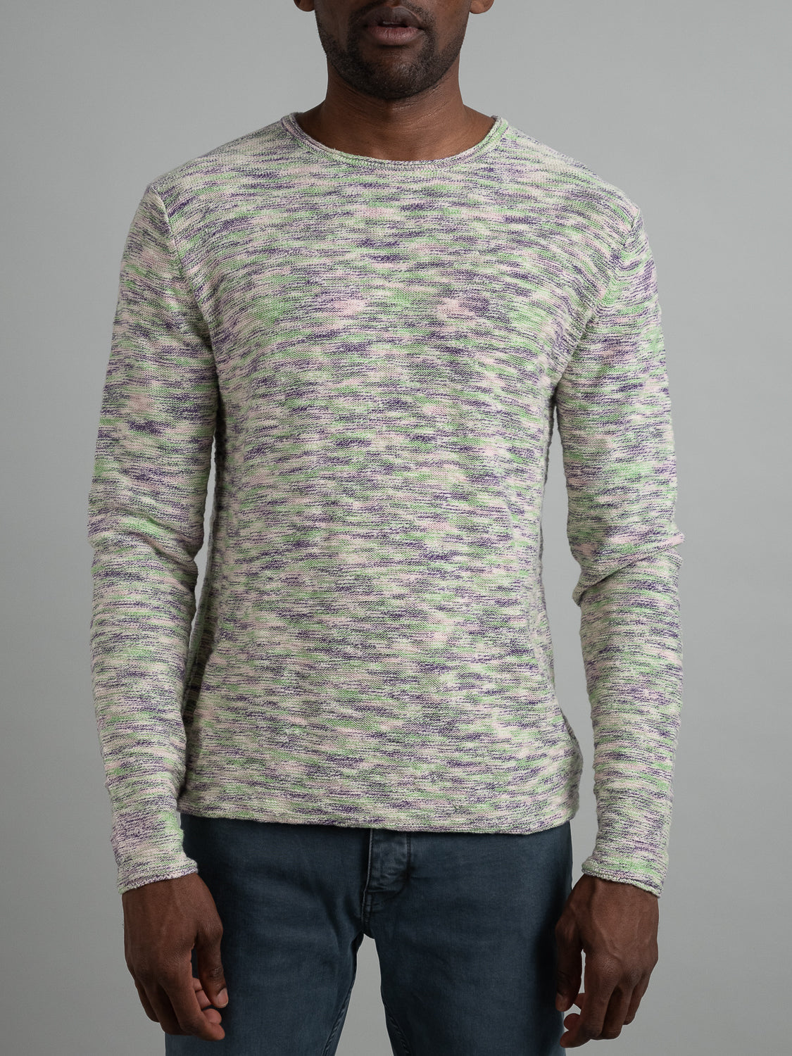 The ID Menswear Havana Slub Yarn Sweater Tee, in multicolored shades of green, pink, and gray, exudes premium quality against a plain gray backdrop. Paired with dark pants, this long-sleeve piece embodies effortless casual wear and is artfully centered on the upper body.