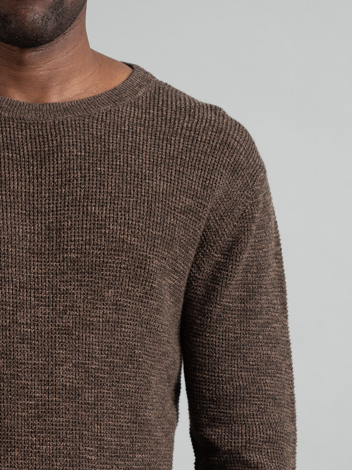 Against a plain gray background, someone wears the Oslo Waffle Knit Sweater by ID Menswear, cropped to reveal only the shoulders and upper chest. Their head and lower body remain unseen.