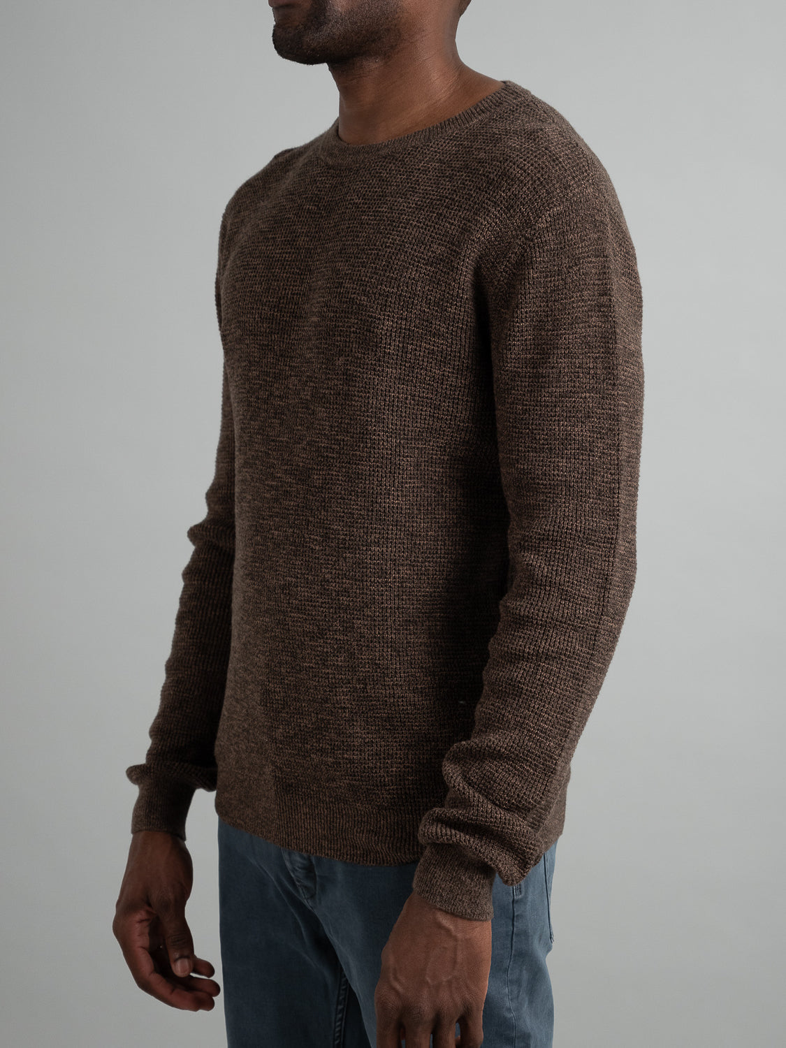 Someone is wearing an Oslo Waffle Knit Sweater by ID Menswear in brown with gray pants, standing neutrally against a plain background, emphasizing the casual outfit.