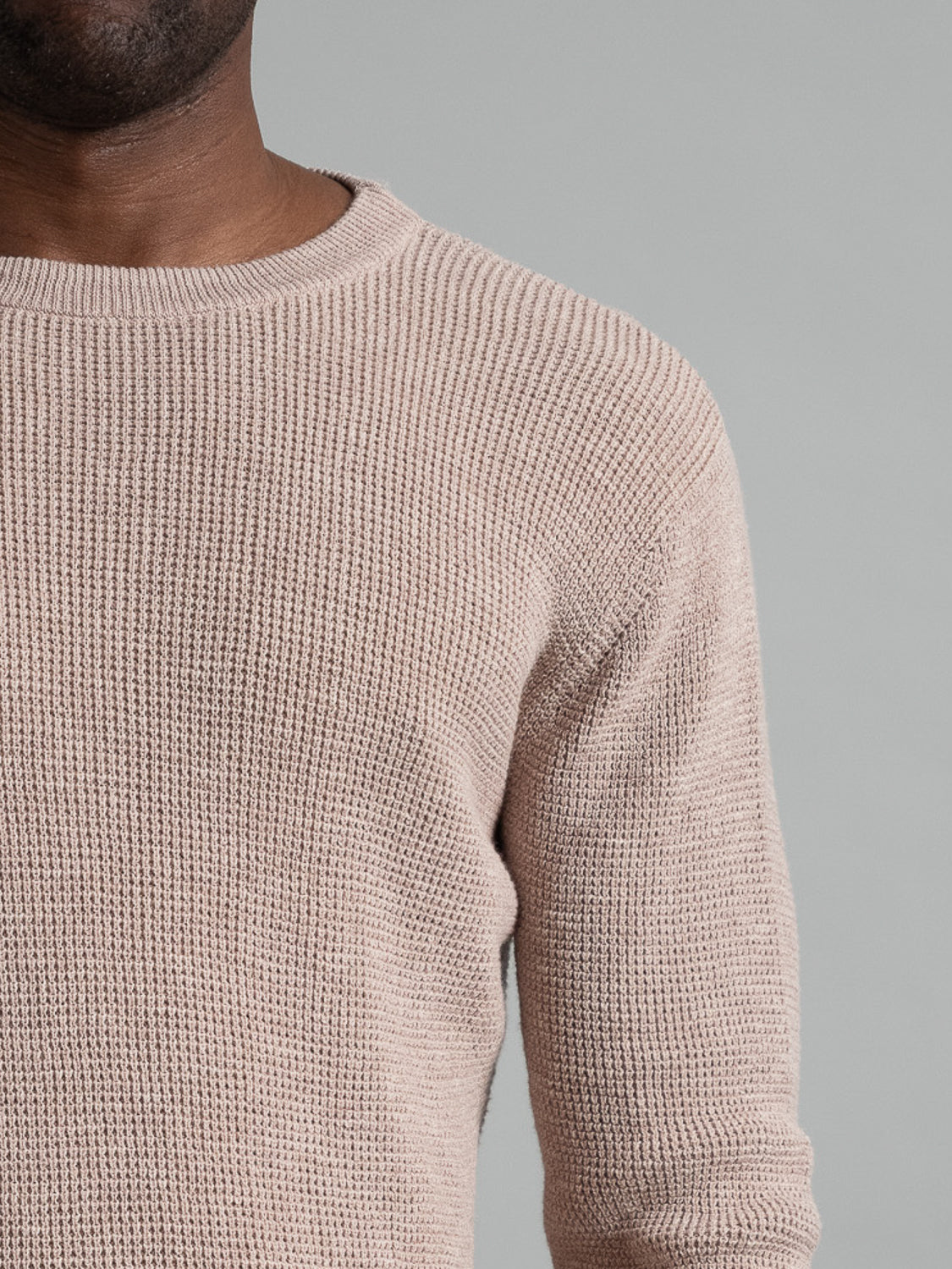 A person wears the Oslo Waffle Knit Sweater by ID Menswear against a plain gray backdrop, highlighting the texture and details of this beige casual cotton piece, focusing on the upper torso and shoulder.