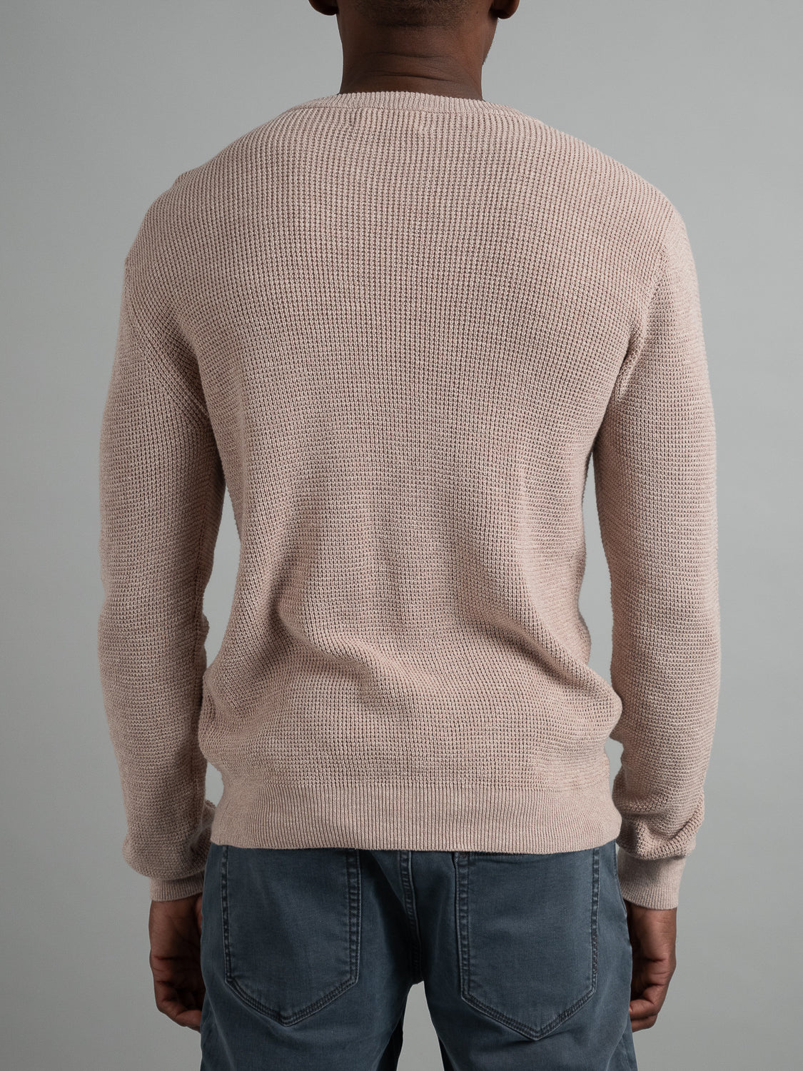A person stands with their back to the camera against a gray background, wearing the Oslo Waffle Knit Sweater by ID Menswear and jeans, perfectly showcasing casual wear at its finest.