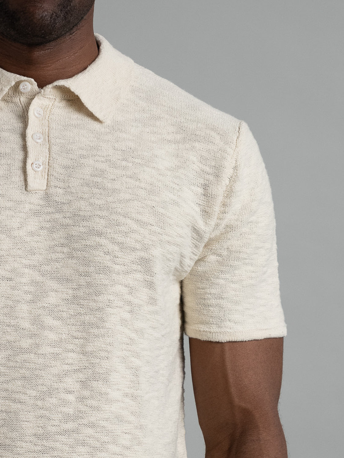 A torso in an ID Menswear Miami Reverse Knit Cotton Polo, cream-colored with a textured design, is set against a gray background. This breathable casual wear features a three-button placket and part of the arm is visible.
