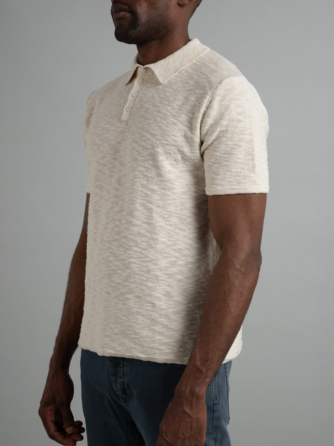 In front of a gray backdrop, someone wears the Miami Reverse Knit Cotton Polo by ID Menswear. This short-sleeve, light beige shirt has a textured cotton-knit and buttoned collar. Ideal for casual outings, it pairs effortlessly with dark pants while providing a breathable and comfortable fit.