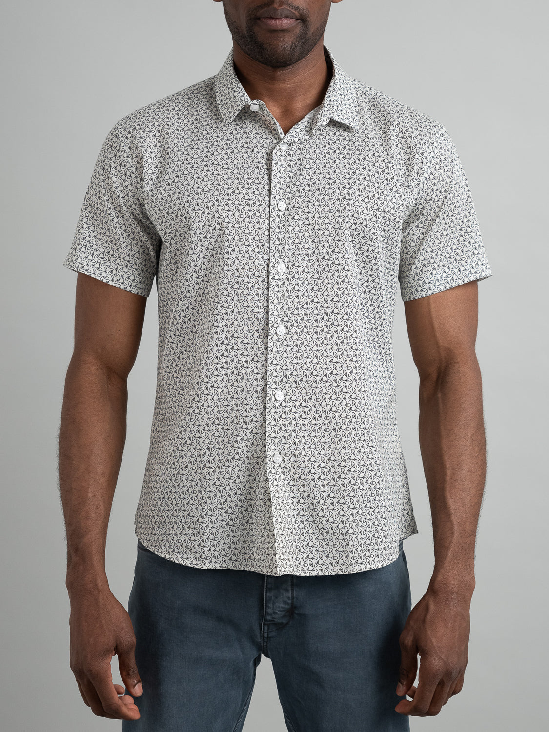 A person wearing the ID Menswear Laurel Short Sleeve Cotton Printed Shirt, known for its slim fit and vibrant design, pairs it with dark pants against a neutral backdrop. Only their torso and arms are shown.