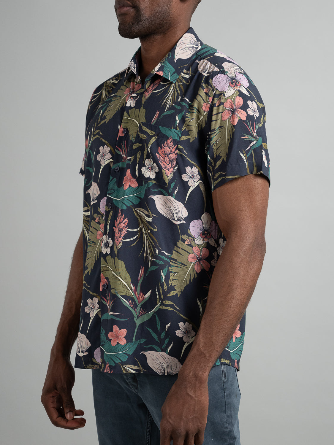 A man stands against a plain background wearing the Kauai Short Sleeve Printed Rayon Shirt by ID Menswear, featuring vibrant floral prints.