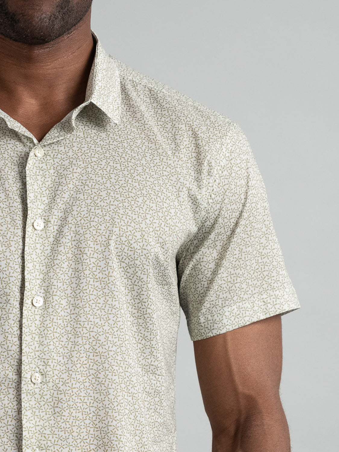 Close-up of someone wearing the ID Menswear Anise Short Sleeve Cotton Printed Shirt, a slim fit with a subtle geometric pattern. The light-colored shirt has a small, repeating design, perfectly complementing the plain gray background and highlighting the sleek look of one torso side.