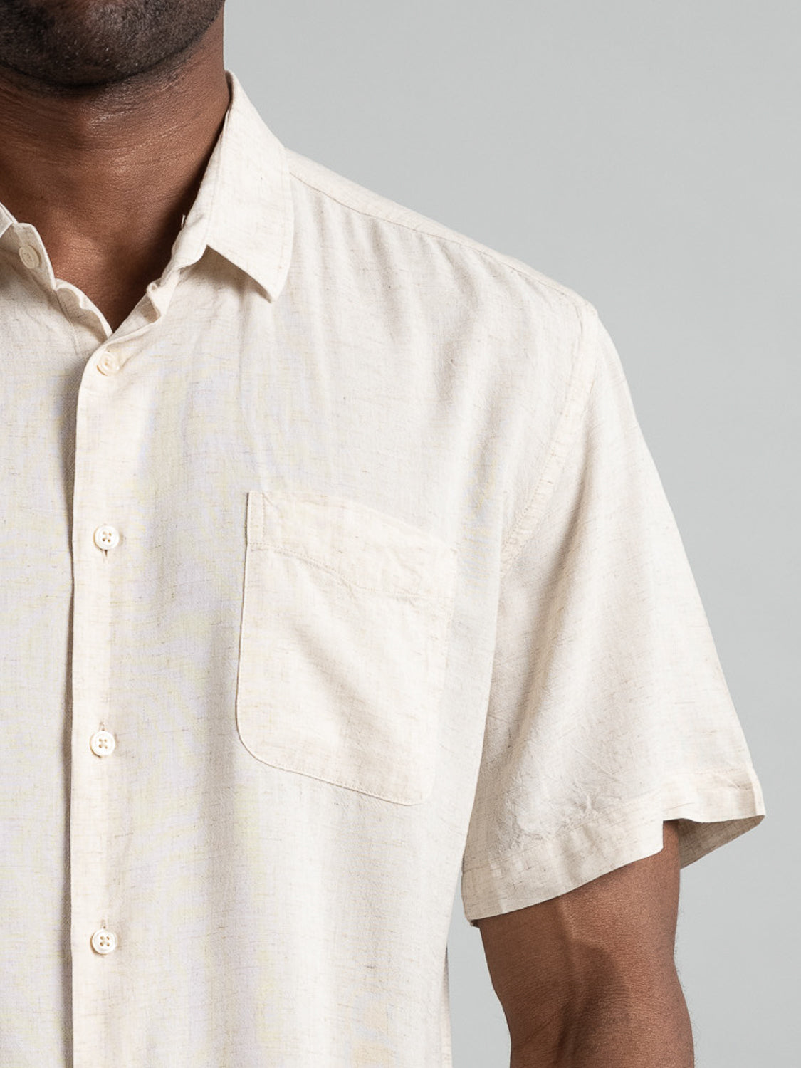 Cropped image of a person in the Maharishi Rayon Linen Short Sleeve Shirt by ID Menswear, featuring a single breast pocket against a plain gray background. Crafted from a rayon linen blend for a lightweight feel.