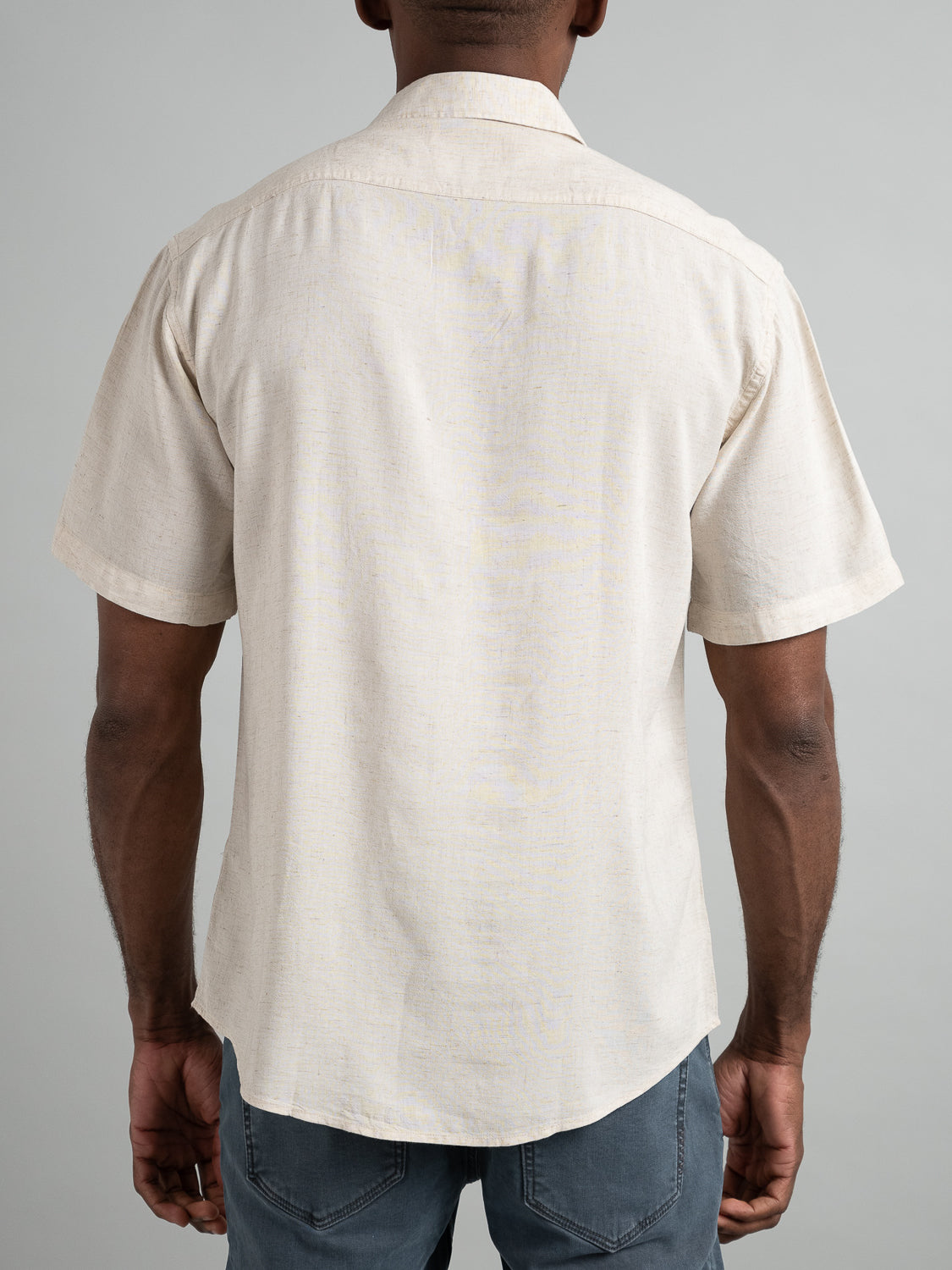 Rear view of a person wearing the Maharishi Rayon Linen Short Sleeve Shirt by ID Menswear and gray jeans against a neutral background, showcasing style and comfort.