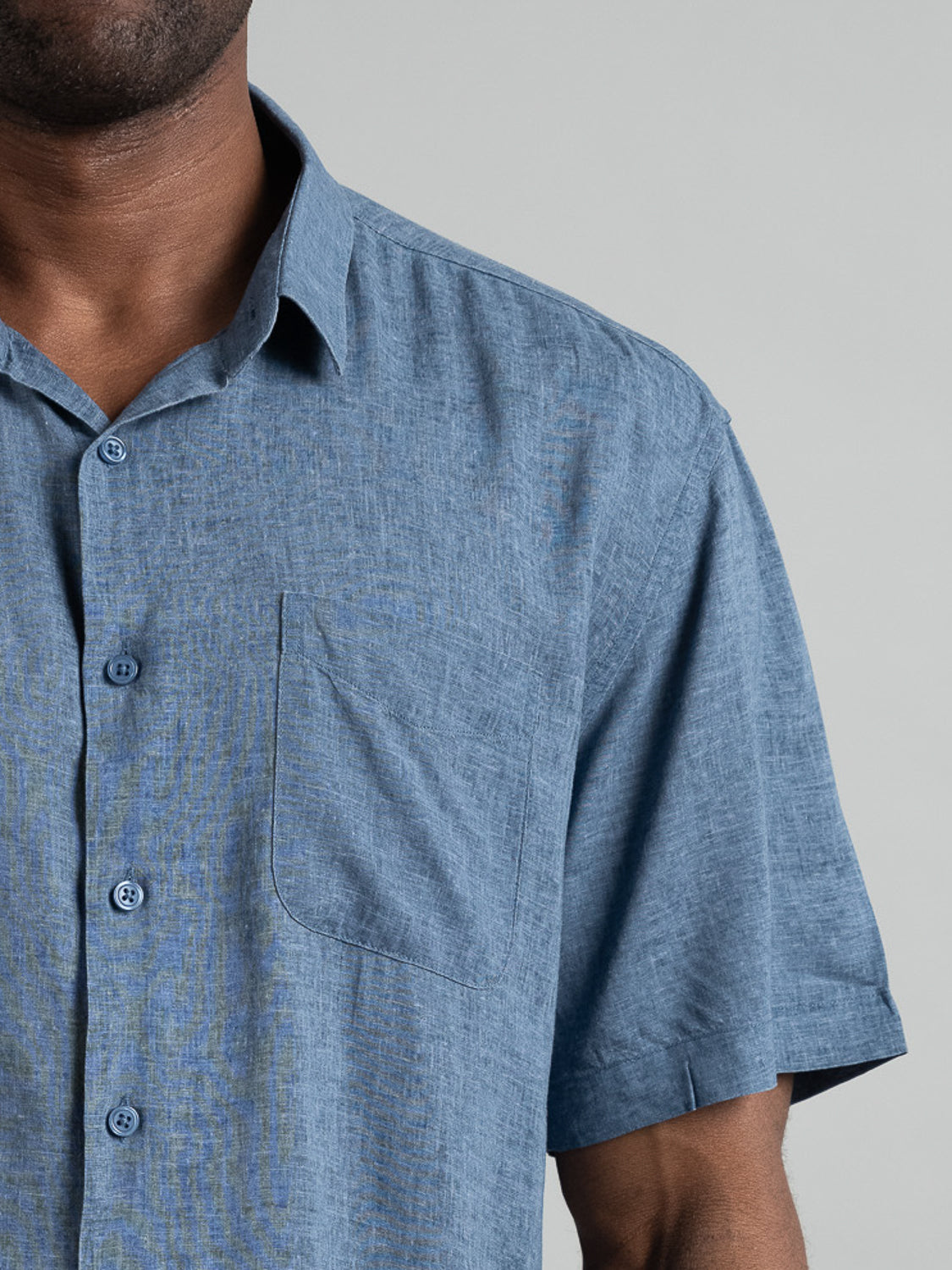 Close-up of an upper body wearing the Maharishi Rayon Linen Short Sleeve Shirt by ID Menswear. This lightweight blue shirt features a textured pattern, short sleeves, button-up front, and a left-side pocket.