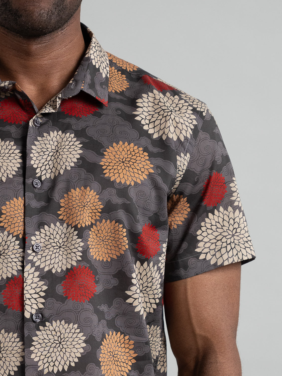 The Tibet Short Sleeve Cotton Printed Shirt by ID Menswear features large, bold white, red, and gold flowers on a dark gray background. It has a classic collar and buttons.