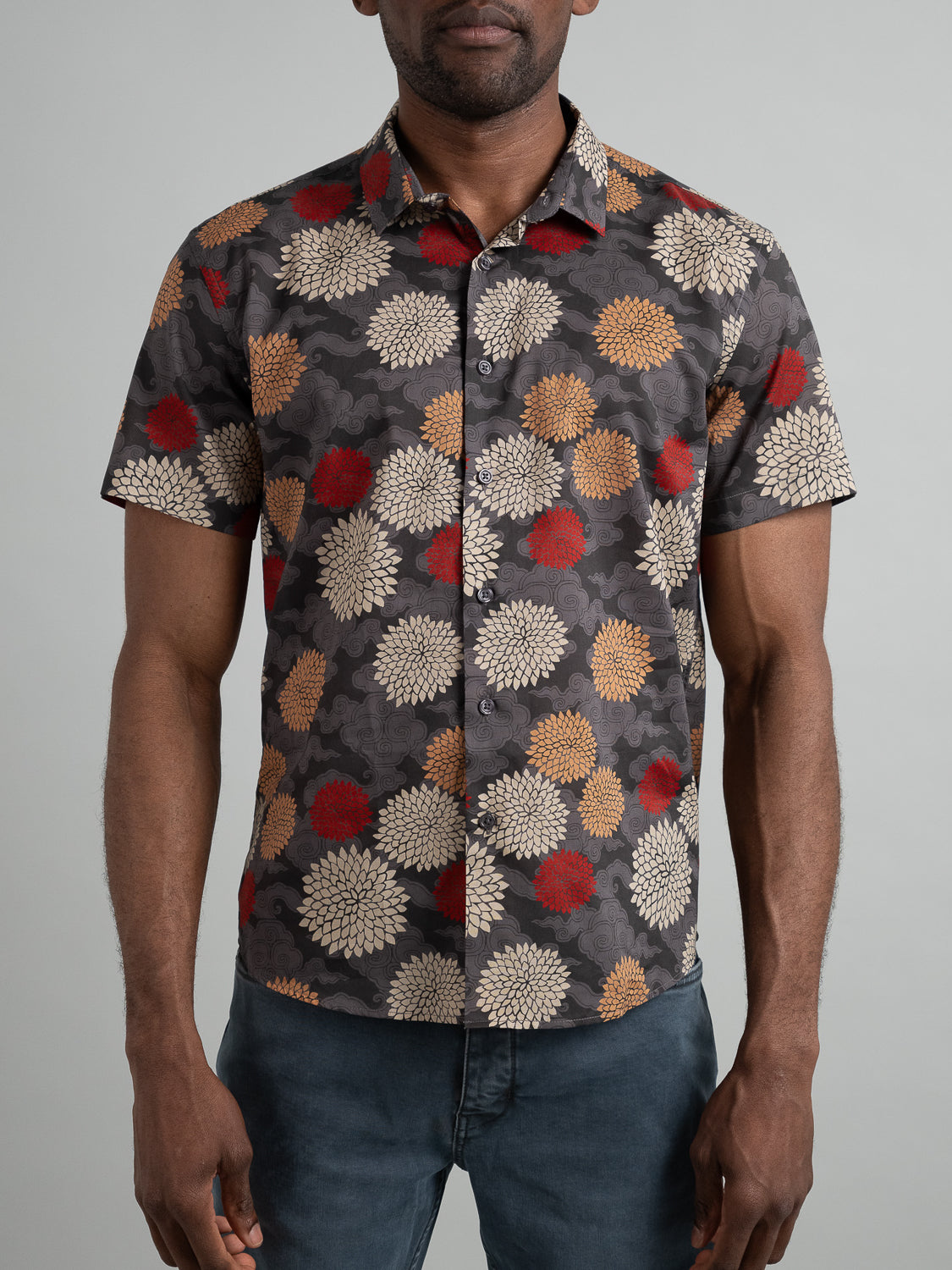 An individual sports the ID Menswear Tibet Short Sleeve Cotton Printed Shirt, featuring vibrant red and beige floral designs on a dark background, matched with dark pants against a plain light gray backdrop.